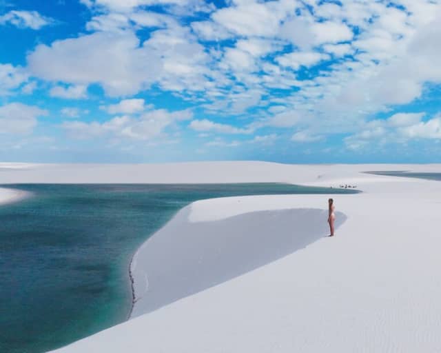 Mulher em pé sobre uma duna branca acima de uma lagoa azul-turquesa nos Lençóis Maranhenses, sob céu azul Mulher em pé sobre uma duna branca acima de uma lagoa azul-turquesa nos Lençóis Maranhenses, sob céu azul