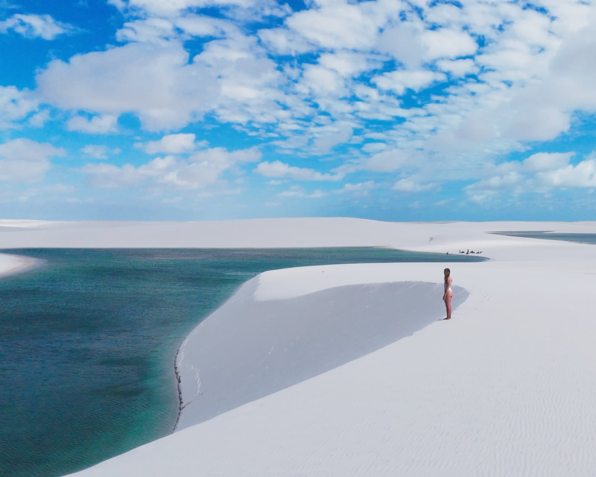 Femme debout sur une dune blanche au-dessus d’une lagune turquoise dans les Lençóis Maranhenses, sous un ciel bleu Femme debout sur une dune blanche au-dessus d’une lagune turquoise dans les Lençóis Maranhenses, sous un ciel bleu