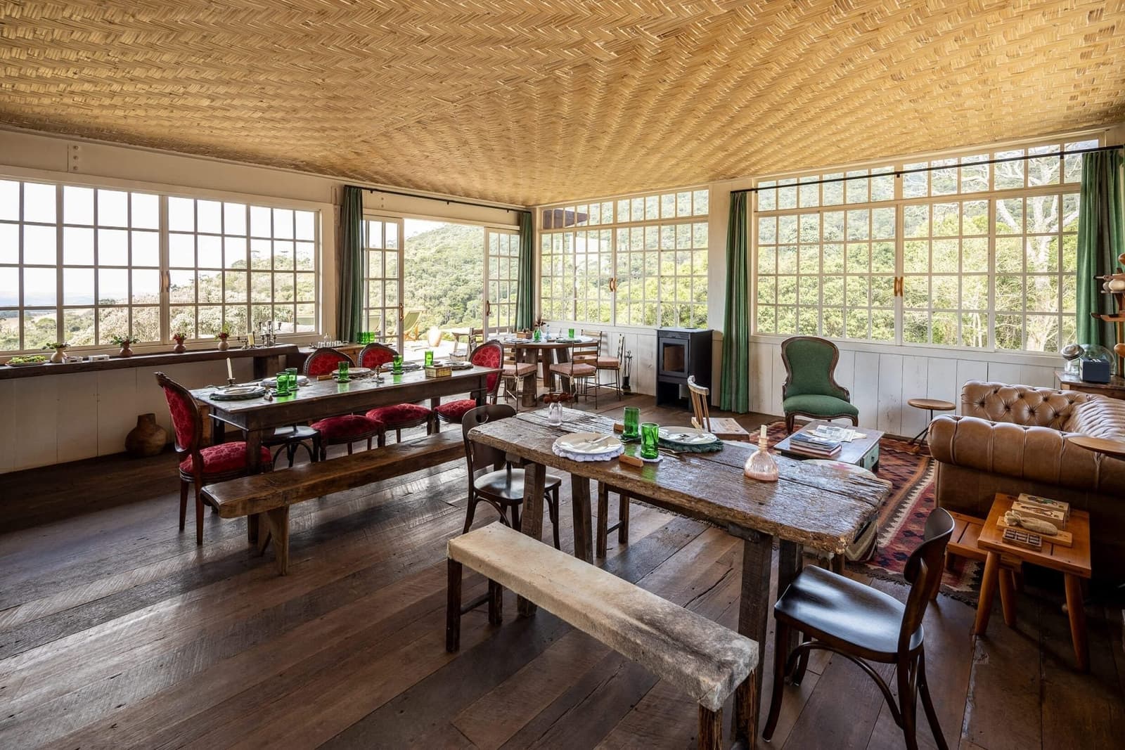 Mittagessen mit Waldsicht, rundum und ohne Ausrede, draußen zu sitzen. Rustikaler Speisesaal der Engenho Lodge im Ibiti Project mit Holztischen aus altem Holz, roten Samtstühlen, Steinbänken, grünem Glas, gewebter Decke und raumhohen Fenstern mit Blick in den Wald