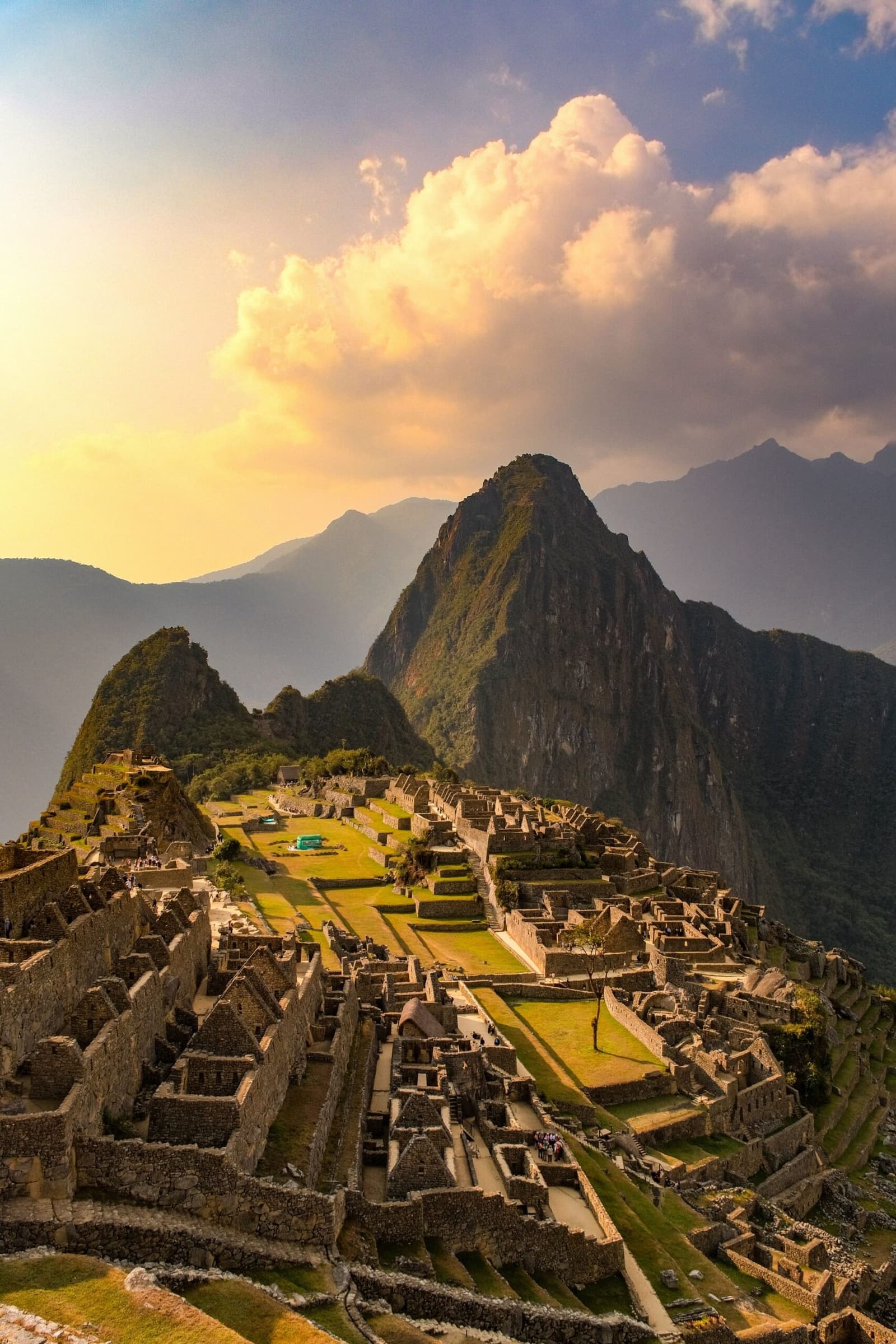 Late light, ancient stone, and a city that took centuries to build and one afternoon to fall in love with. Aerial view of the Machu Picchu citadel on a luxury Machu Picchu tour, with stone ruins and green terraces spread across a high ridge and Huayna Picchu peak rising behind under a warm golden sky