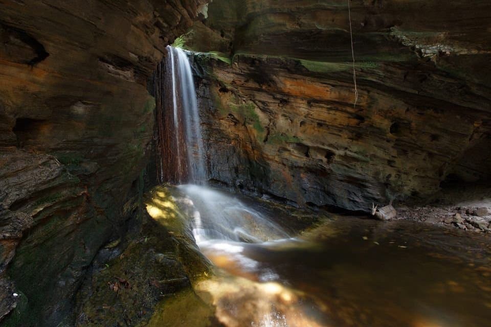 Tief im Fels verborgen, hält dieser Wasserfall seinen eigenen Rhythmus. Ein schmaler Wasserfall fällt durch geschichtete Sandsteinwände in einer geschützten Felsschlucht des Ibiti-Projekts und sammelt sich in einem stillen, bernsteinfarbenen Becken
