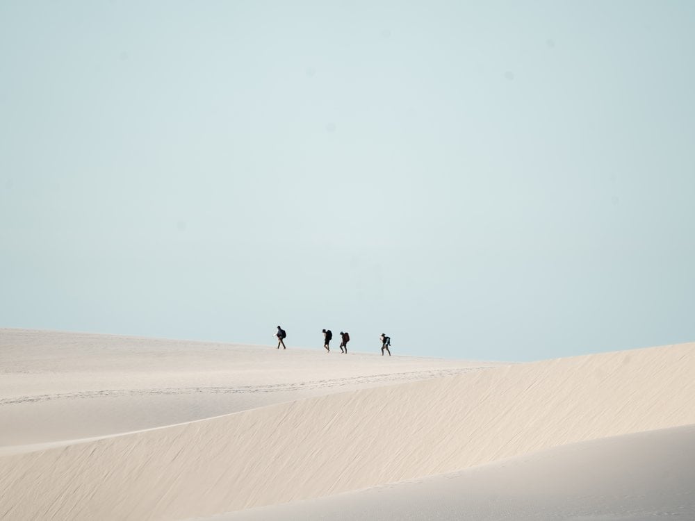 Away from the crowds, close to what matters. Overland tourism focuses on small groups to ensure that a high percentage of revenue stays in local communities. (Credit: Isadora Sá) Small group of hikers crossing the white sand dunes of Lençóis Maranhenses