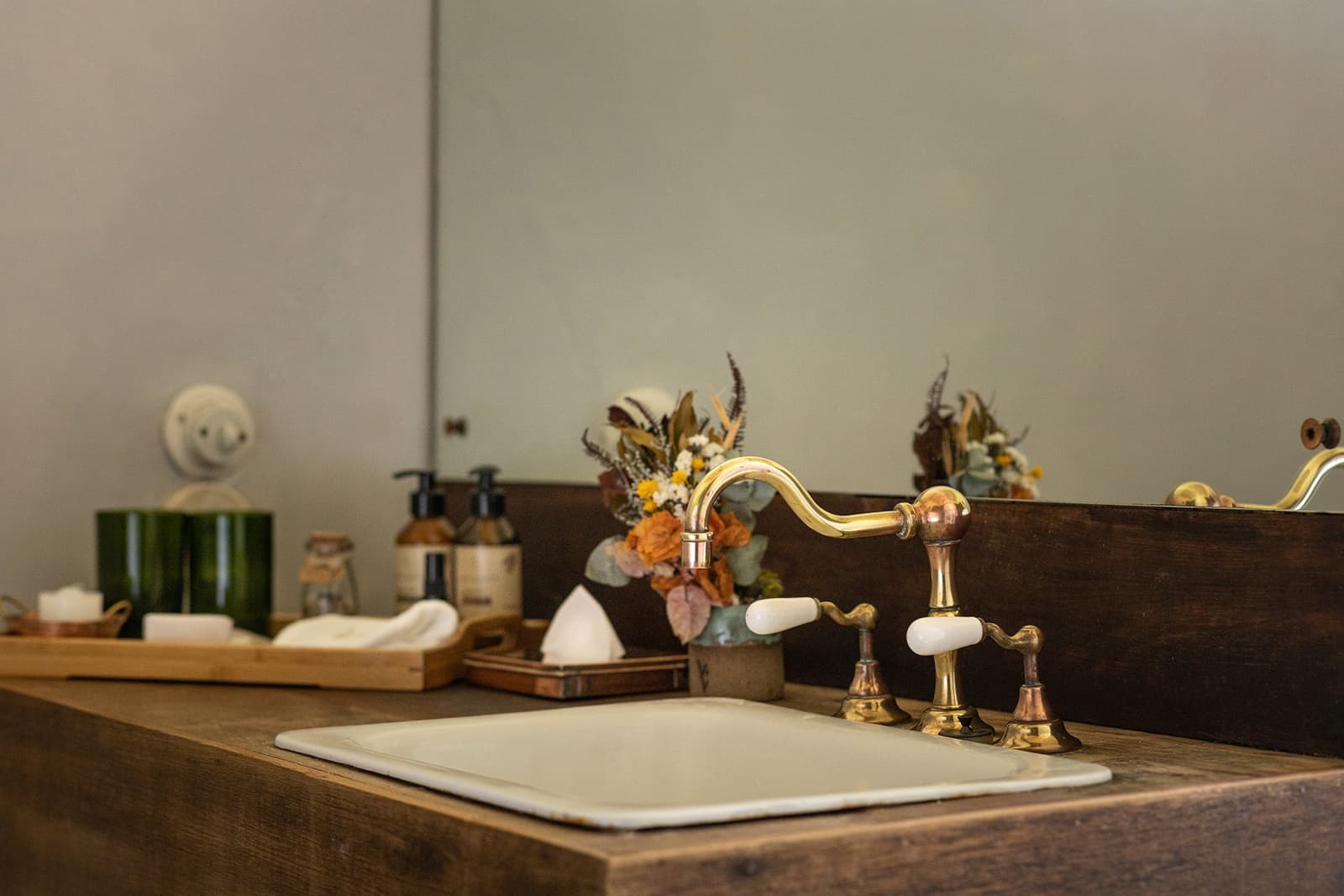 Hier steckt Sorgfalt in jedem Detail, vom Holz bis zum Messing. Photo: Henrique Mangeon Nahaufnahme eines weißen Keramikwaschbeckens in einer dunklen Holzarbeitsplatte mit messingfarbenen Vintage-Wasserhähnen und einem kleinen Trockenblumenarrangement im Bad der Engenho Lodge des Ibiti Project