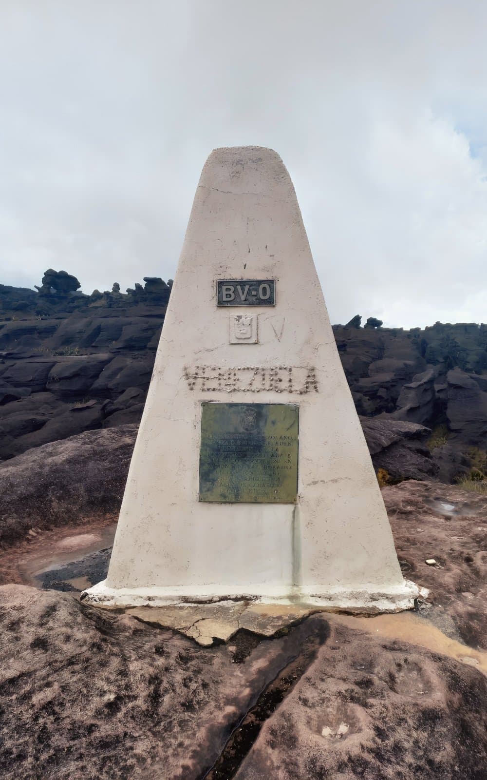 Três países, um obelisco de concreto e muitos dias de caminhada para chegar até aqui. Marco fronteiriço piramidal branco com as inscrições BV-0 e Venezuela sobre rocha escura antiga no Ponto Triplo durante a expedição ao Monte Roraima