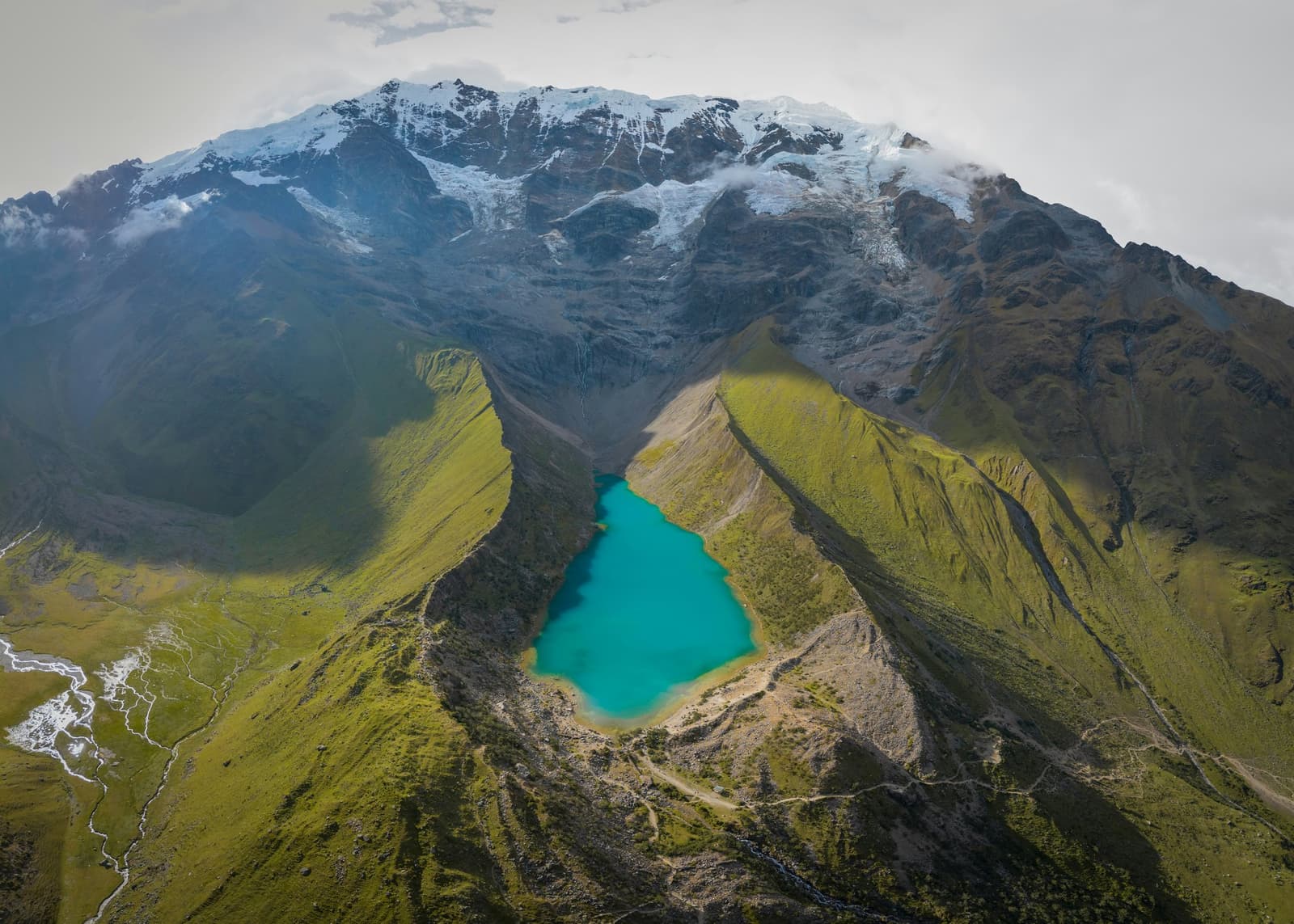 That color is not a filter. The glacier above makes it happen. Aerial view of a turquoise glacial lake nestled in a high-altitude Andean valley below a snow-capped glacier on a luxury Machu Picchu tour through the Peruvian highlands