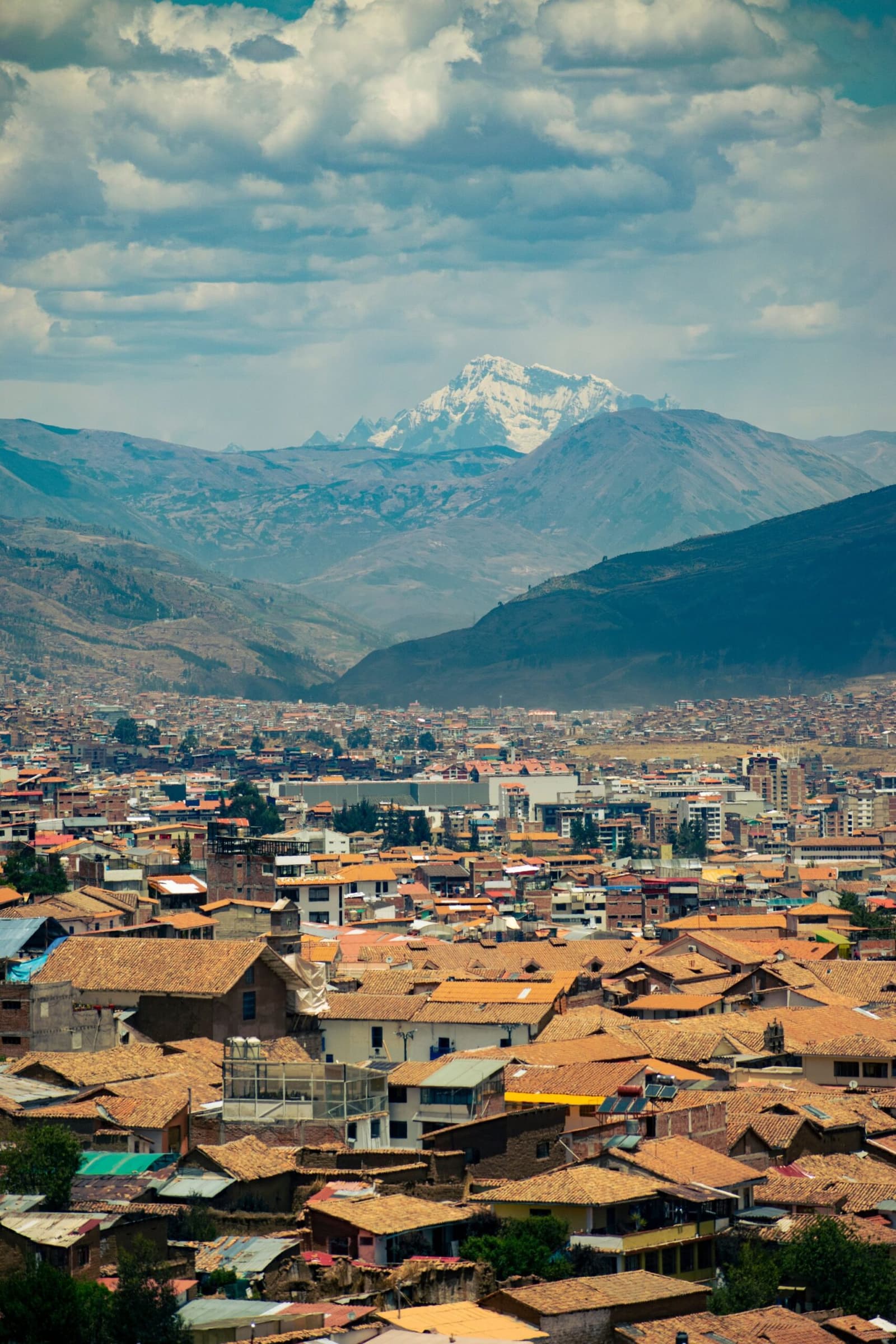 Cusco from above: terracotta as far as you can see, and a glacier keeping watch at the back. Aerial view of Cusco's terracotta rooftops spreading across the valley on a salkantay tour, with a snow-capped Andean peak rising behind the city under a partly cloudy sky