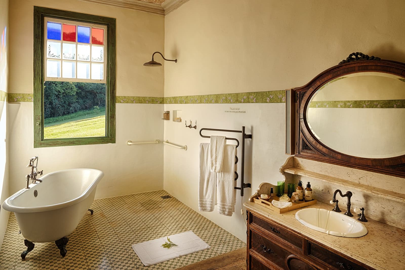 Freistehende Wanne, Garten vor dem Fenster, kein Plan für den Nachmittag. Photo: Henrique Mangeon Freistehende Badewanne neben einem Buntglasfenster mit Gartenblick im Ibiti Project Lodge-Badezimmer, mit geschnitztem Holzwaschtisch, Marmorplatte und antikem Ovalspiegel