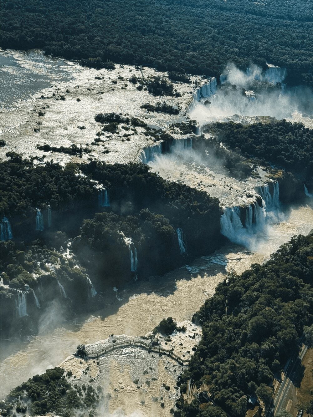 Photo: Marina Zvada Aerial view of Iguazu Falls, with dozens of waterfalls dropping into the gorge and a walkway over the river
