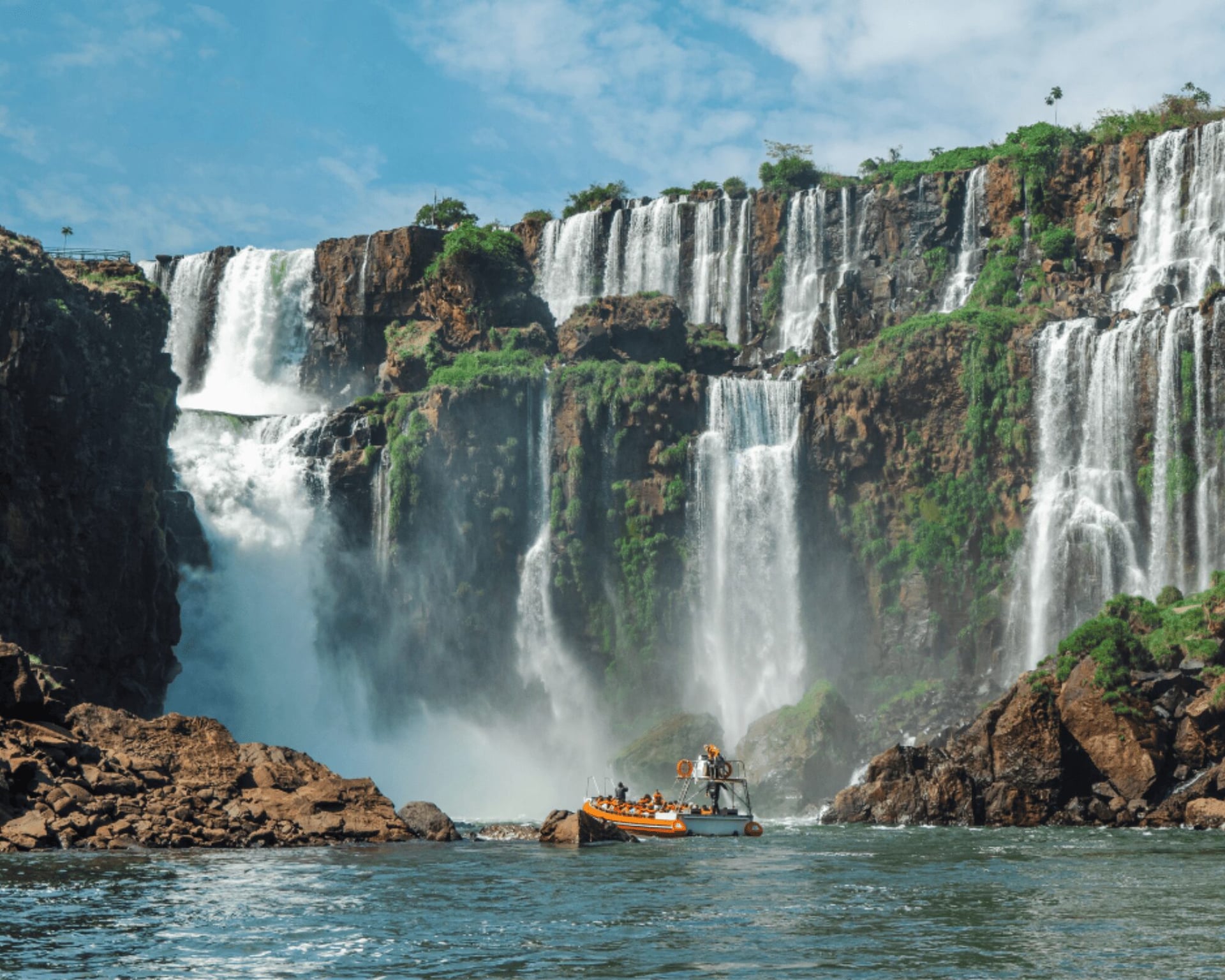 Boat tour approaching the base of Iguazu Falls under a blue sky Boat tour approaching the base of Iguazu Falls under a blue sky