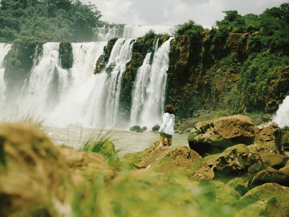 Photo: Belmond Hotel das Cataratas Traveler standing on the rocks at the base of the waterfalls at Iguazu Falls