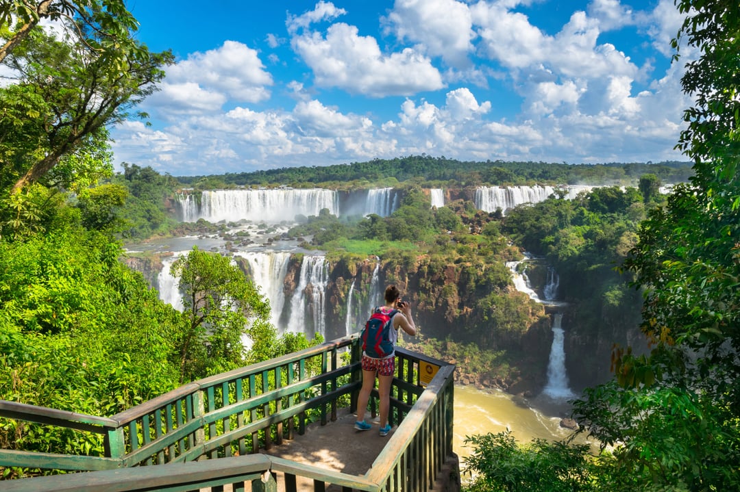 Photo: NidoHuebl Traveler photographing Iguazu Falls from a viewpoint on the walkway, surrounded by rainforest