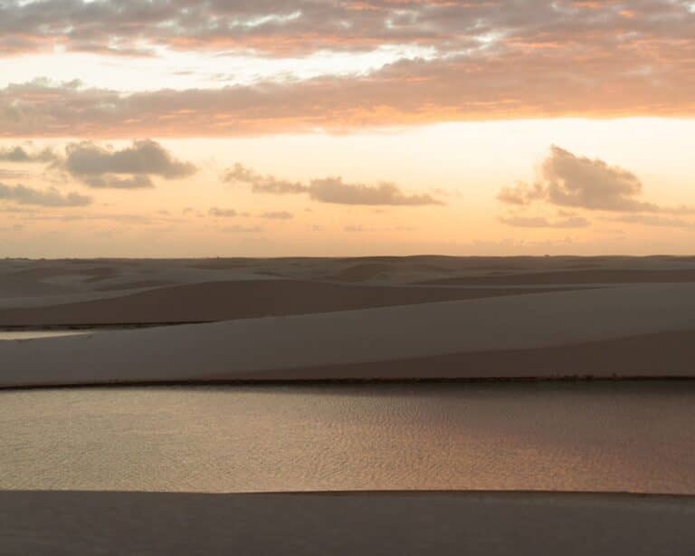Ciel rose au coucher du soleil sur les dunes de sable blanc et une lagune d’eau de pluie aux Lençóis Maranhenses