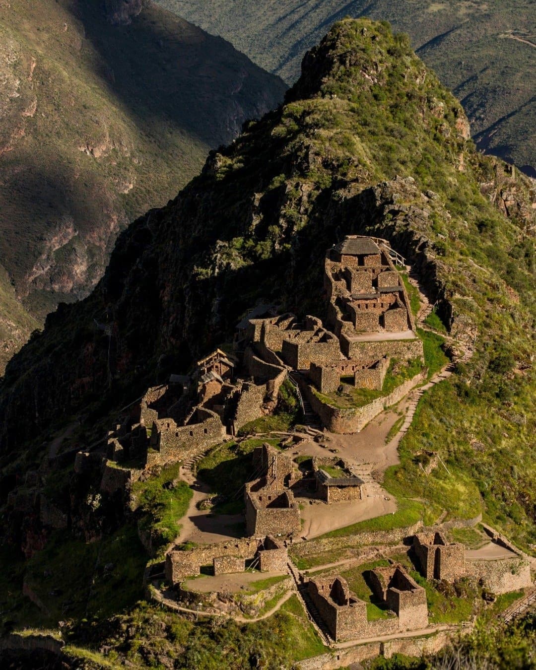 Centuries of stonework, still holding their ground on the ridge. Aerial view of ancient Inca stone ruins cascading down a steep Andean mountain ridge, surrounded by green cloud-forest slopes and deep valleys on an andes trek route in Peru