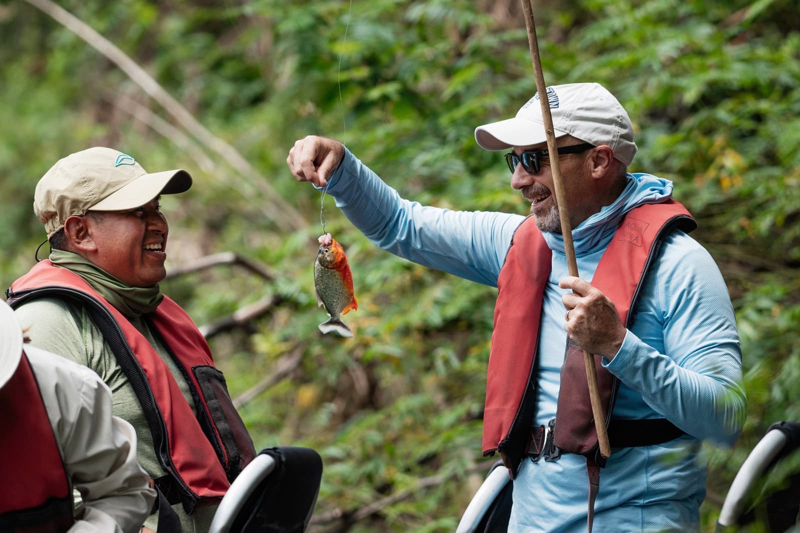 First piranha. The guide's reaction says it all. Photo: Daniel Silva Yoshisato A smiling traveler holds up a small piranha on a line during an aria amazon cruise excursion, while a laughing local guide looks on from the skiff, dense green jungle in the background