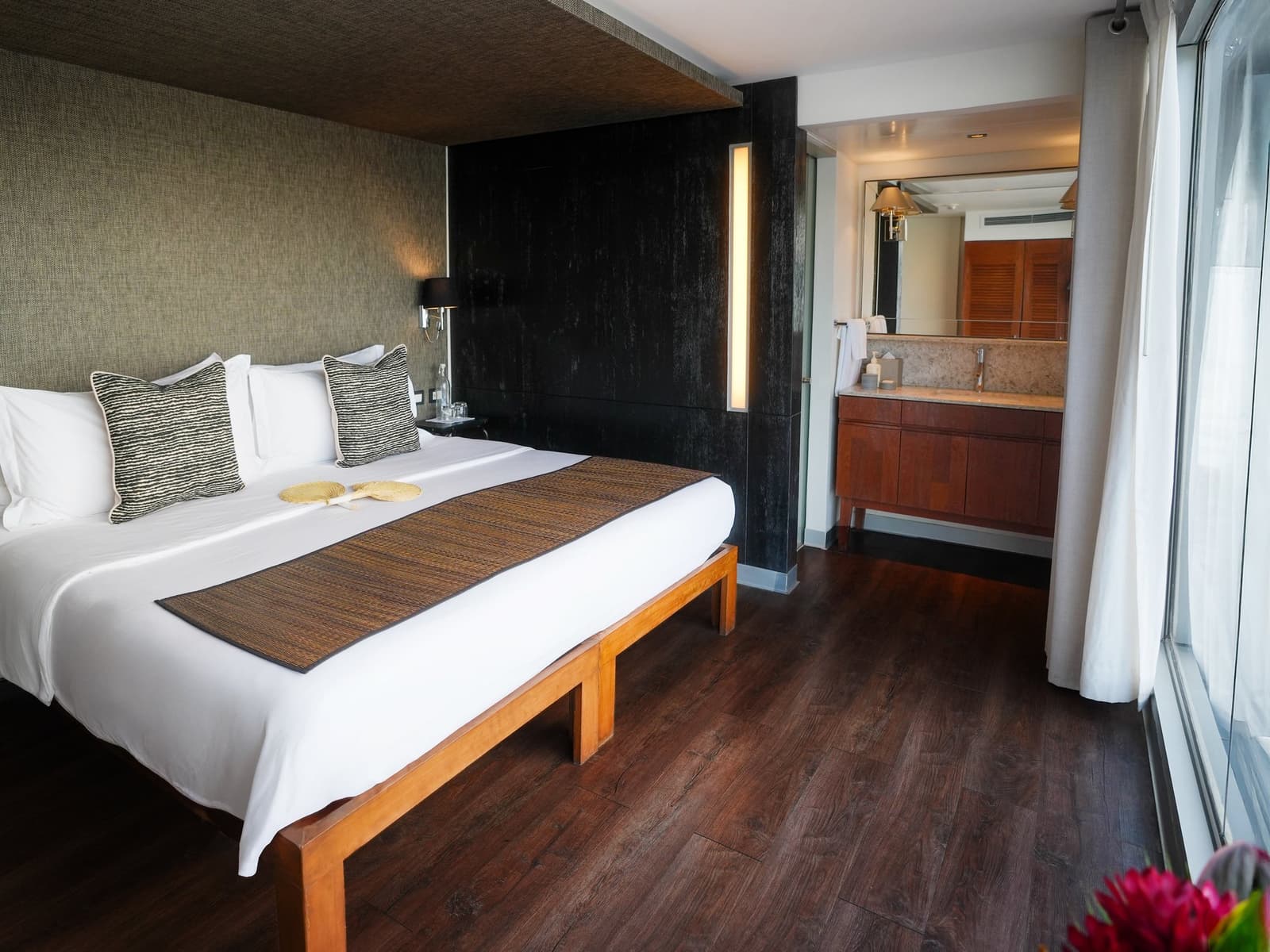 Crisp white linen, warm wood, and the river just outside the glass. Photo: Francois Moreau King bed with woven throw pillows and a bamboo runner on the Aria Amazon cruise, with an open-plan vanity area and floor-to-ceiling curtains beside a panoramic window