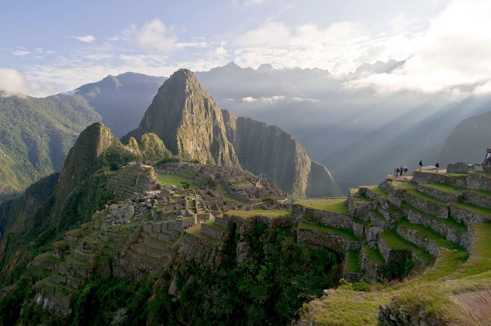 Five days of walking earn you this view. Worth every step. Panoramic view of Machu Picchu citadel on the off-the-beaten-path Salkantay trek, with Inca stone terraces in the foreground, Huayna Picchu peak rising behind the ruins, and low clouds drifting through the surrounding Andean mountains