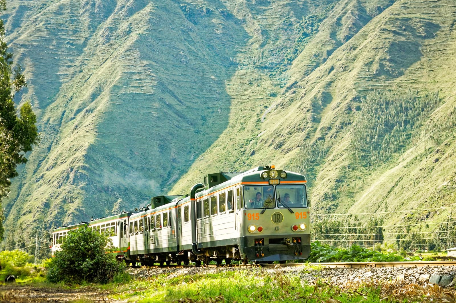 Neste trecho de trilhos, o cenário faz o trabalho todo. O trem IR número 915 percorre um vale andino verde e íngreme com encostas montanhosas aterraçadas ao fundo, na rota do trek Salkantay até Machu Picchu