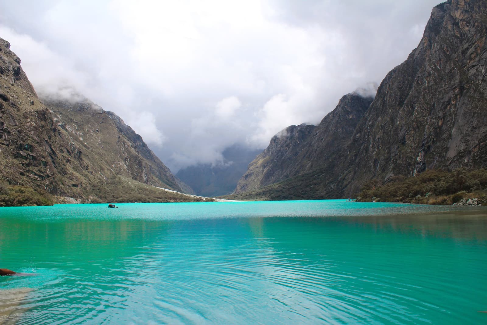That colour is real, and it stops people mid-sentence every time. Vivid turquoise glacial lake on the santa cruz trek flanked by steep rocky Andean peaks with low cloud filling the valley beyond
