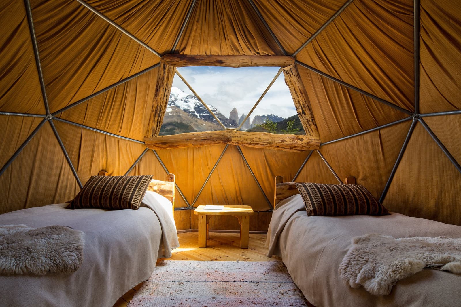 Duas camas, uma janela e as torres ali, esperando por você. Photo: Standard Dome Interior de um domo geodésico no Torres del Paine W Trek, com duas camas de solteiro com mantas de pele de carneiro, janela rústica de madeira e vista direta para as icônicas torres de granito