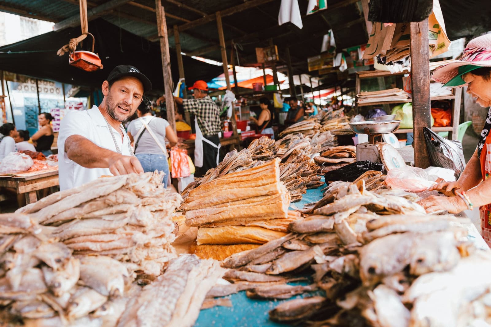 Nauta's market runs on dried fish, quick hands, and loud opinions. A vendor at the Nauta market arranges large piles of dried and salted fish across a busy open-air stall, with other vendors and shoppers visible in the background — a stop on the aria amazon cruise itinerary