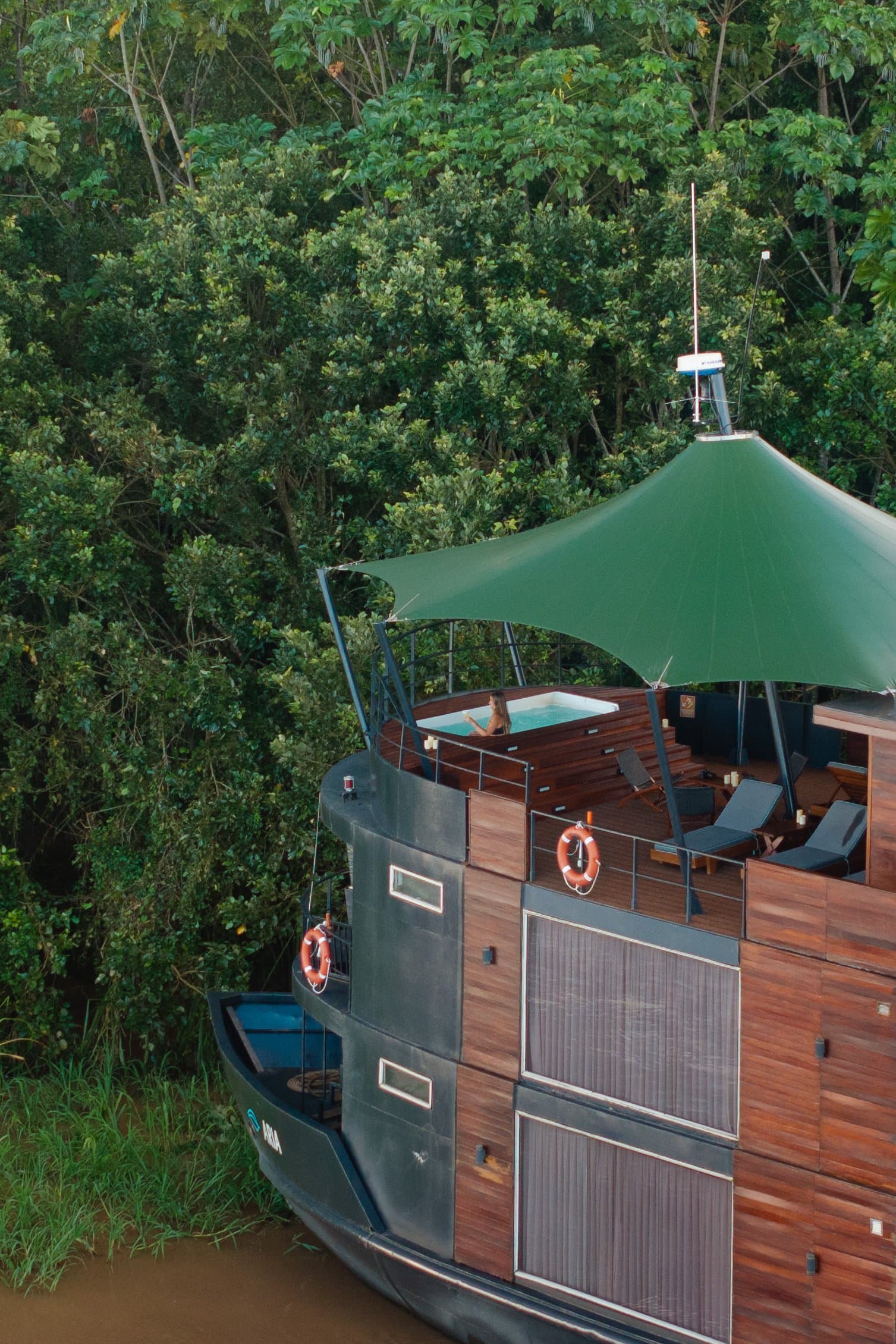 Mergulhar no jacuzzi com a floresta tão perto assim é difícil de acreditar. Photo: Anthony K Do Vista aérea da proa do navio de cruzeiro Aria Amazon atracado junto à densa floresta tropical, com deck superior de madeira, toldo verde, jacuzzi externo e espreguiçadeiras