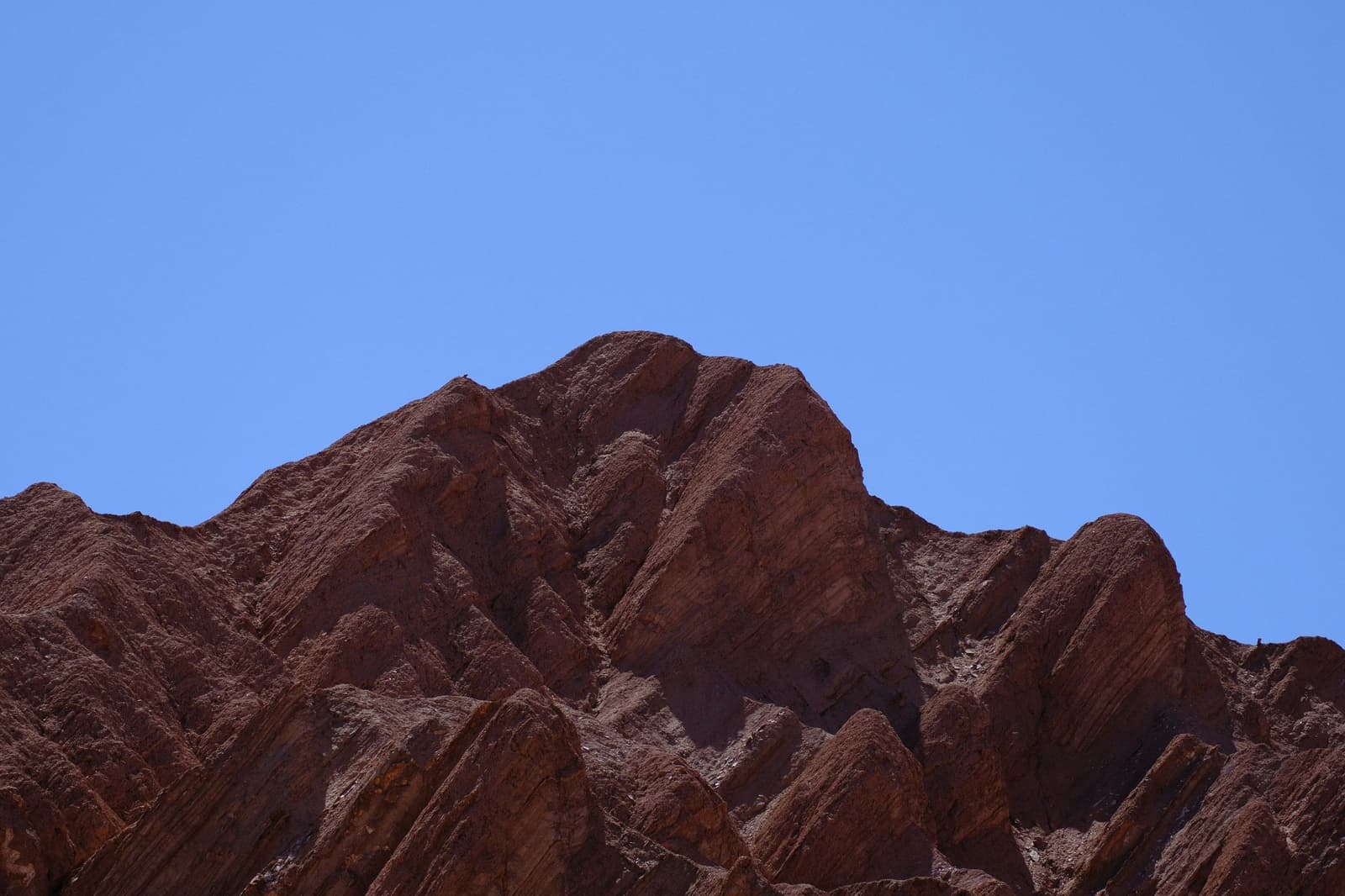 Roca tan antigua no tiene por qué andar con delicadezas. Crestas dentadas de formaciones rocosas de color rojo intenso recortadas contra un cielo azul despejado en el desierto de Atacama
