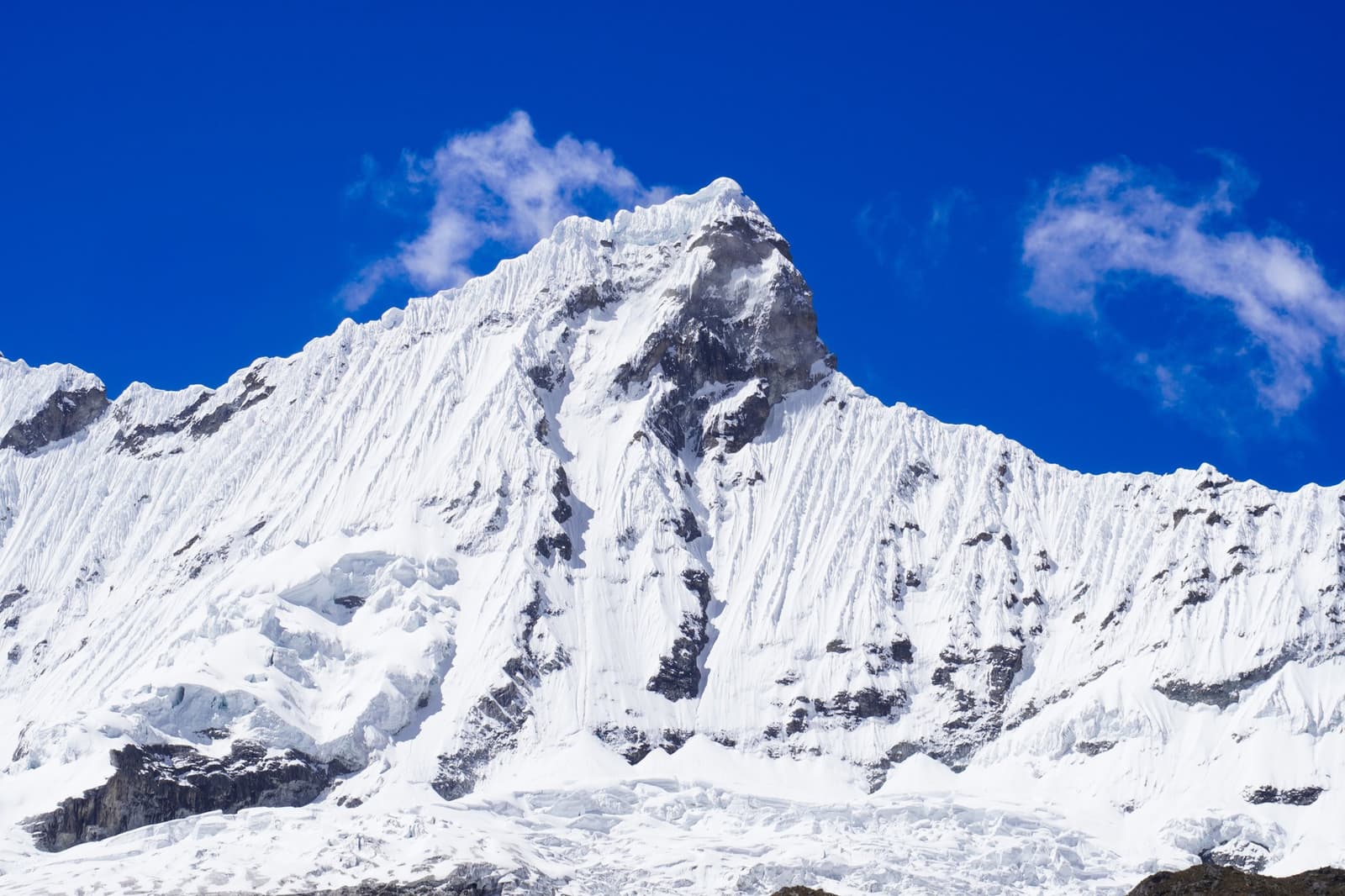 Séculos de gelo esculpiram essas paredes. A montanha não cedeu um centímetro. Um pico fortemente glaciado no circuito Huayhuash se eleva abruptamente sob um céu azul intenso, com faces quase verticais riscadas de neve e rocha exposta no cume.