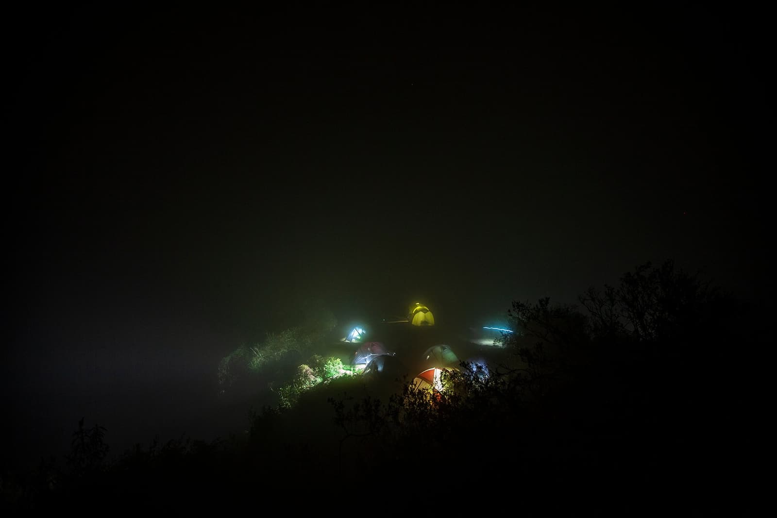 A pocket of light in a whole lot of darkness. Good tents make good trekkers. Glowing tents clustered on a dark hilltop ridge along the Inca Trail to Machu Picchu, wrapped in thick night fog with silhouetted shrubs in the foreground