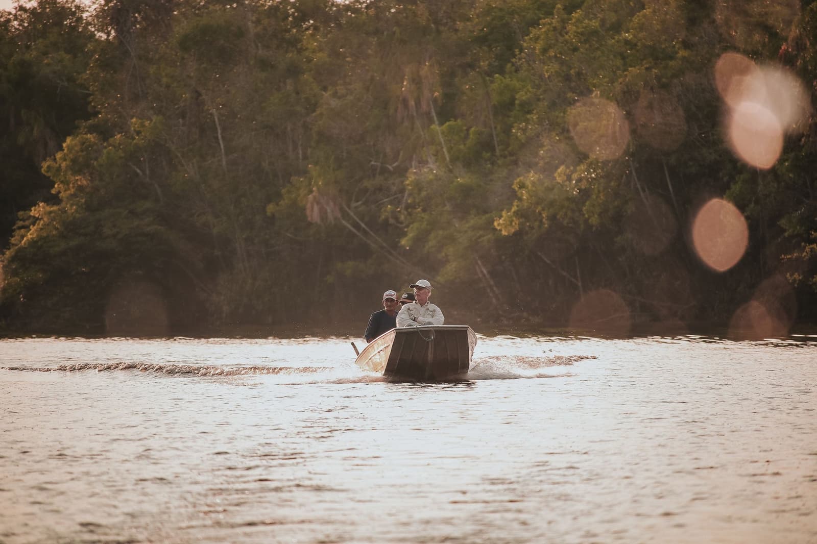 The river doesn't care about your schedule, and honestly, neither does the boat. Photo: JEAN GC Two passengers ride a small motorboat upriver at golden hour on a machu picchu amazon tour, dense riparian forest lining both banks
