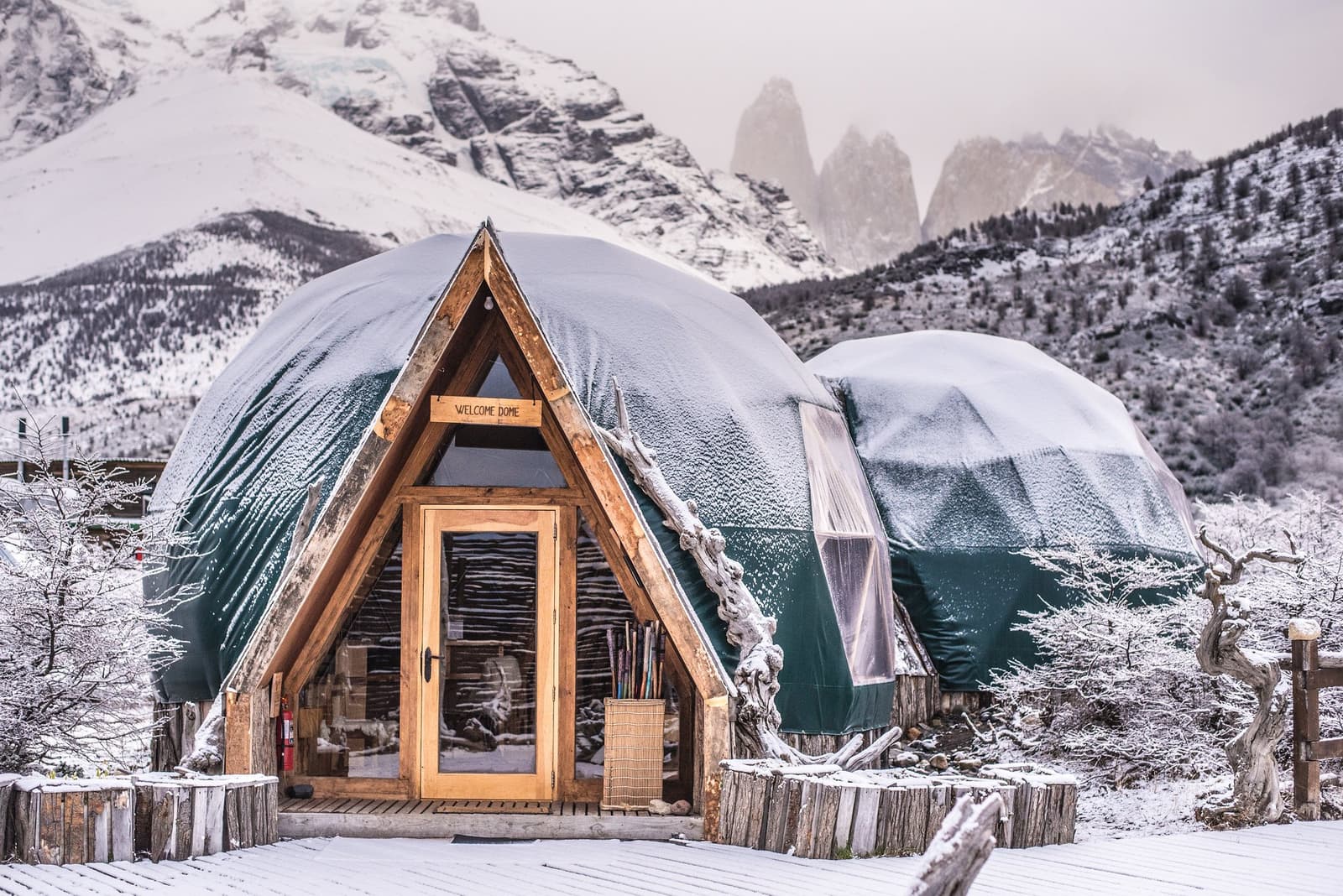 Fresh snow on the domes, the Torres half-hidden in cloud. Not a bad arrival scene. Photo: Welcome Dome Snow-dusted geodesic Welcome Dome at EcoCamp Patagonia with the granite towers of Torres del Paine rising through mist in the background, part of the o trek patagonia o trek in patagonia experience