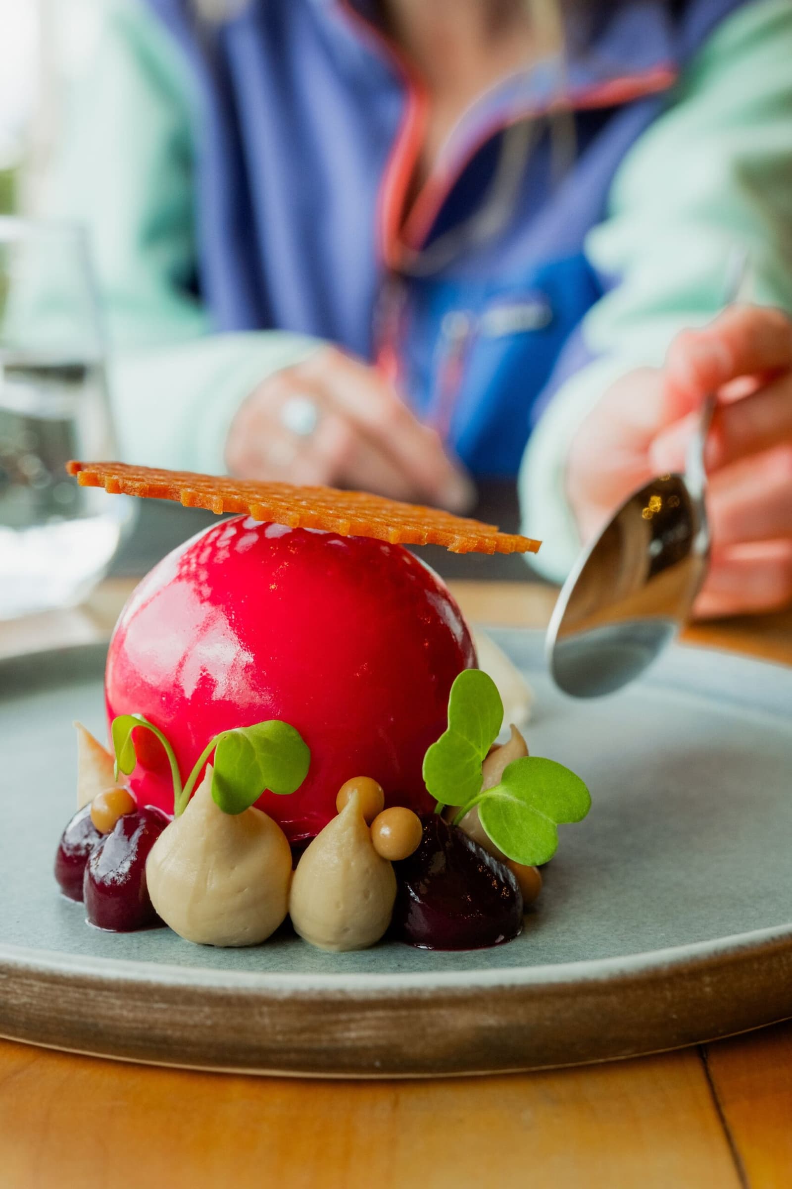Proof that the kitchen here takes dessert just as seriously as the scenery. Photo: Patagonia Camp A glossy crimson dome dessert garnished with cream piped rosettes, dark cherries, fresh microgreens, and a caramel tuile wafer, served tableside at Patagonia Camp restaurant