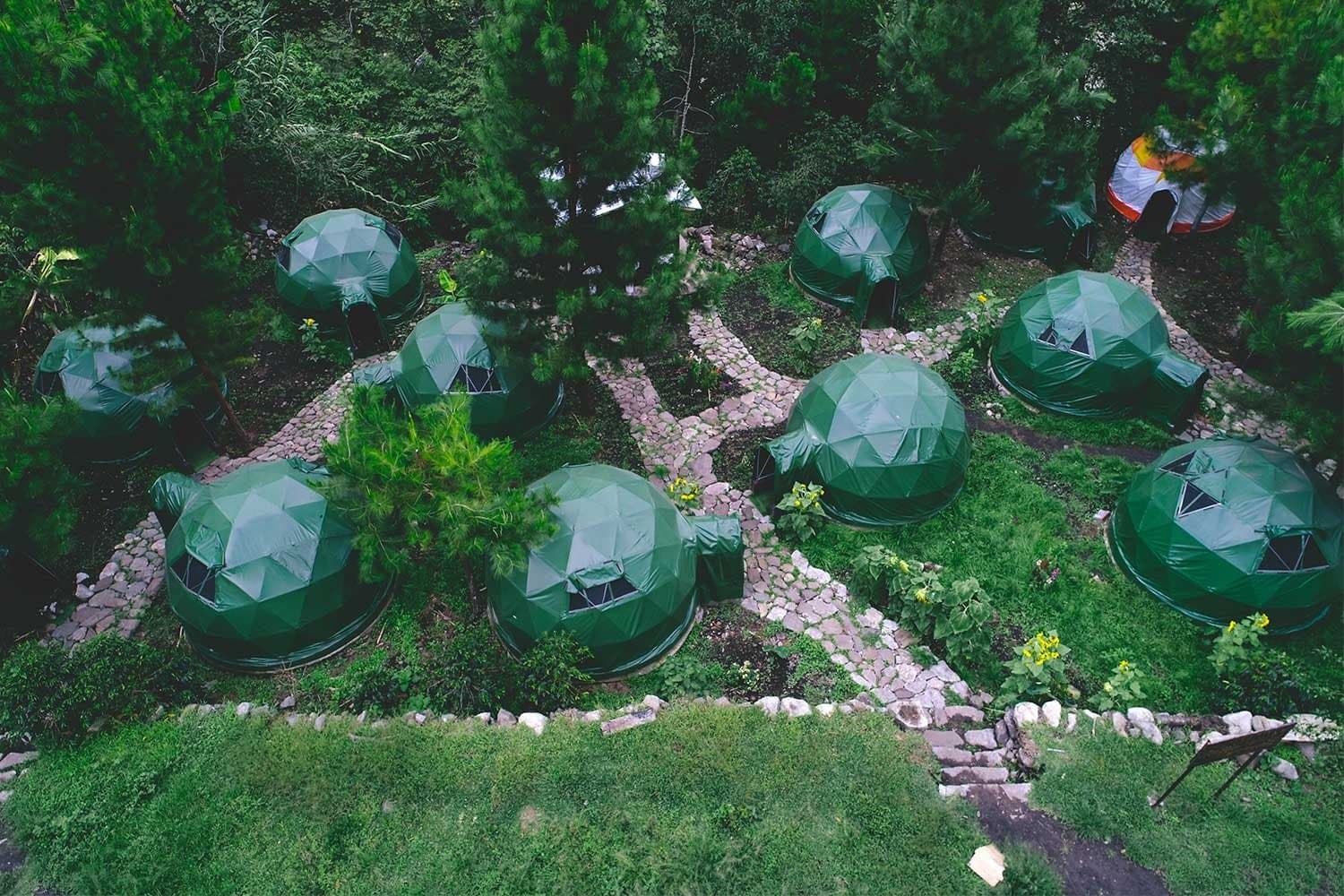 Uma noite na floresta, sem abrir mão da cama quentinha. Photo: Jungle Domes Lucmabamba Vista aérea de múltiplas cúpulas geodésicas verdes conectadas por caminhos de pedra em um jardim florestal exuberante no acampamento da trilha Salkantay em Lucmabamba, Peru