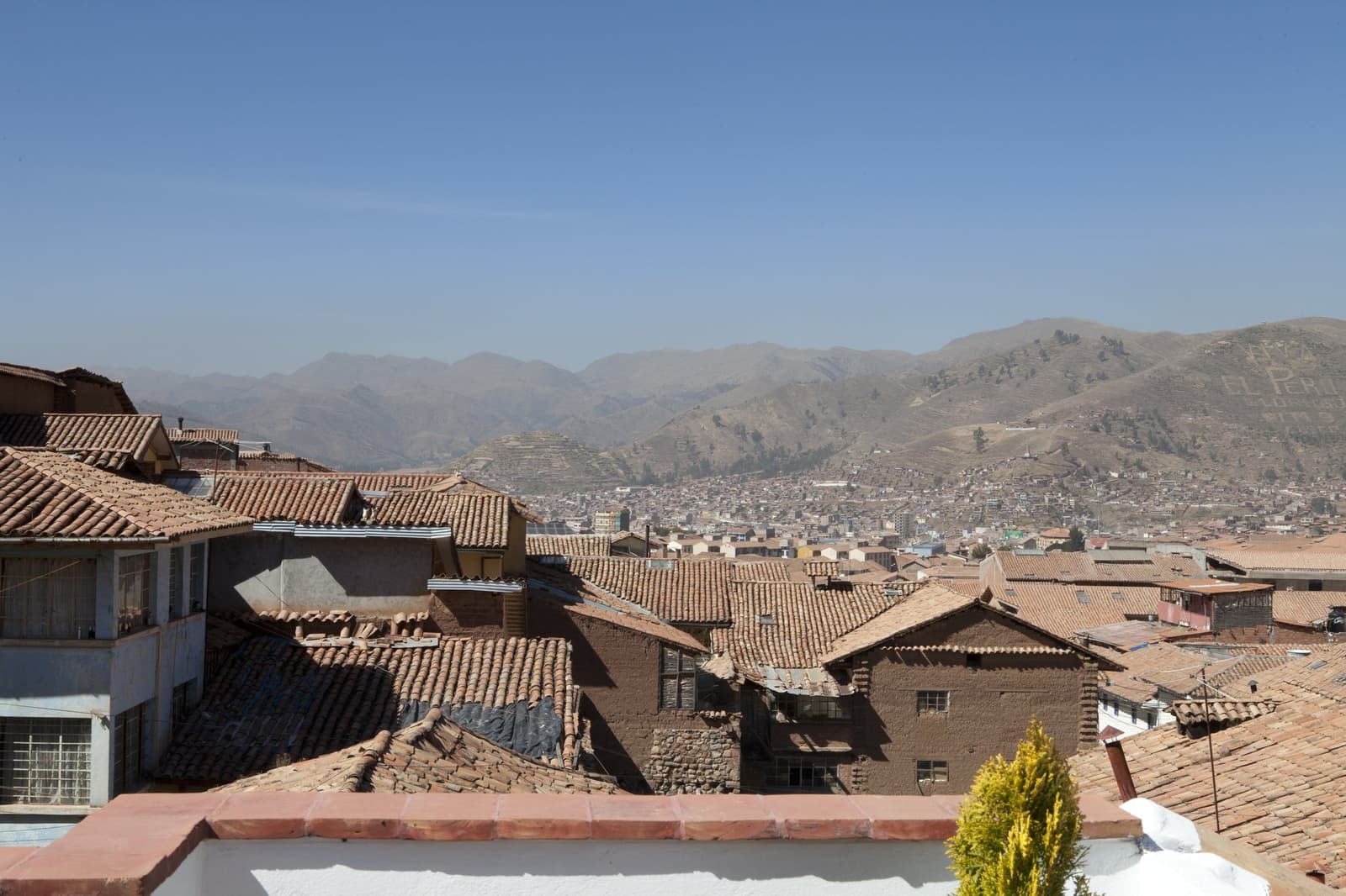 Cusco deitada à sua frente, toda telha vermelha e ar rarefeito, o ritmo certo para começar. Vista panorâmica sobre os telhados de terracota de Cusco com as colinas andinas se dissolvendo na neblina ao fundo, vista de um terraço antes do início do trek Salkantay para Machu Picchu