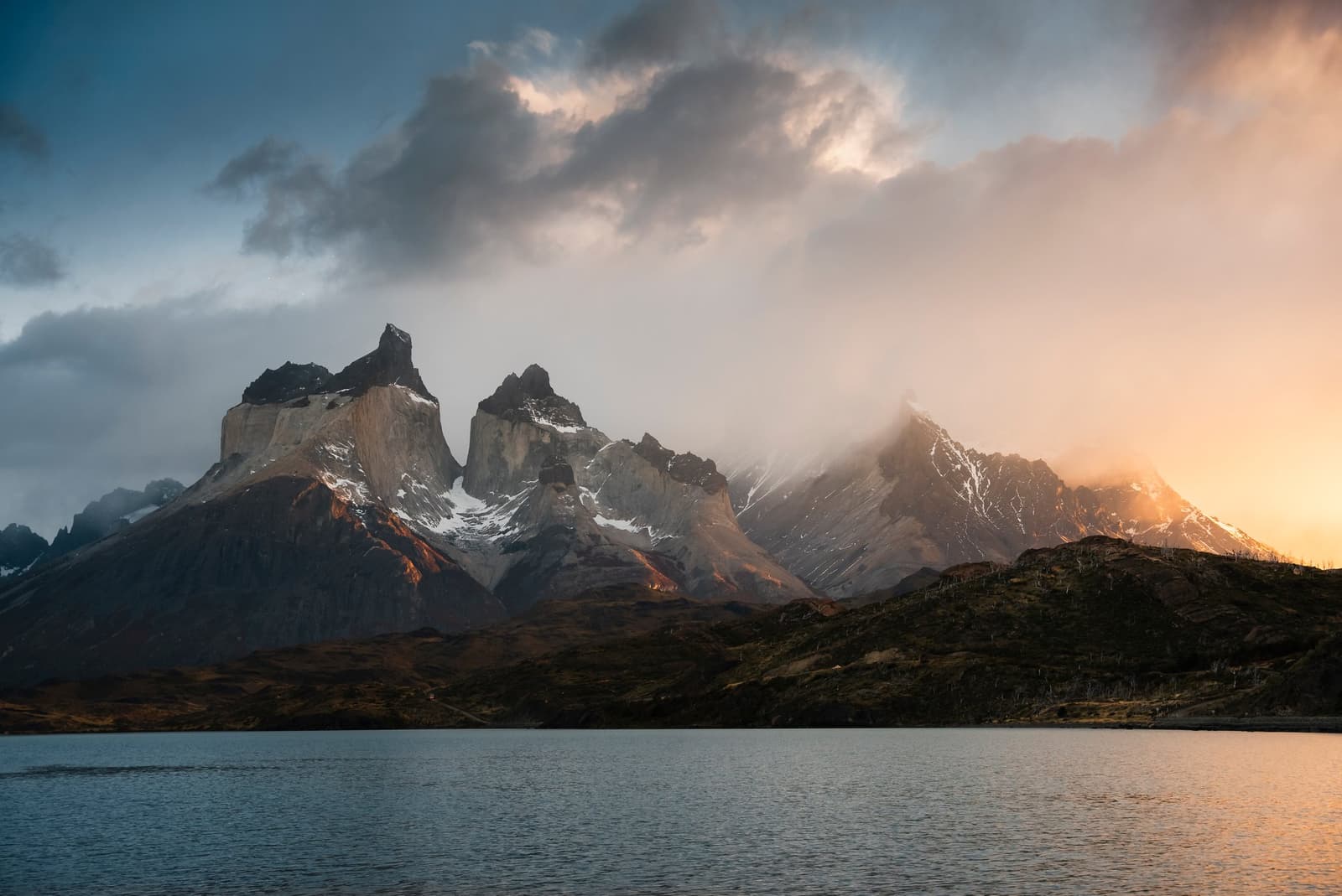 Cuernos del Paine on one of its more cooperative evenings. Don't count on this every night. The jagged twin peaks of Cuernos del Paine rise above a calm lake on the self-guided W Trek, their granite faces lit by a warm orange glow breaking through stormy clouds at dusk
