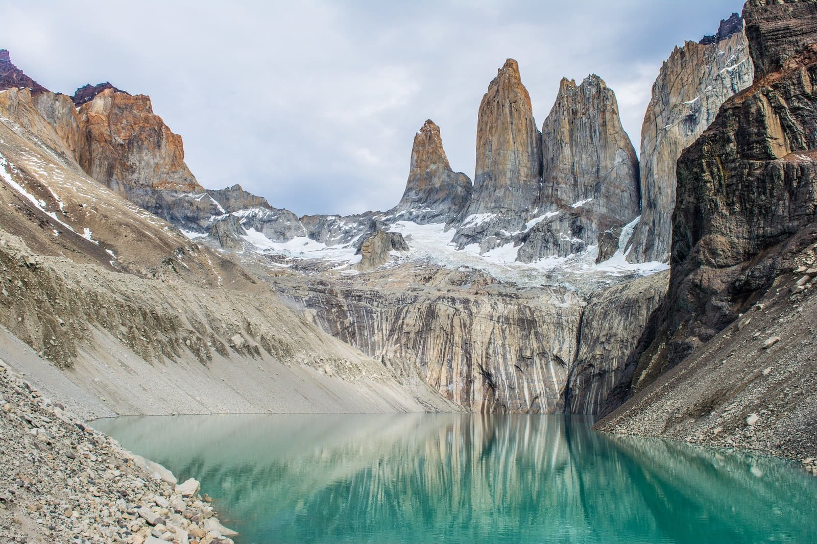Eight hours of trail, and this is what's waiting at the top. Worth every step. Three granite towers of Torres del Paine rising above a glacial moraine with a vivid turquoise lagoon in the foreground, the endpoint of the torres del paine 4 day all inclusive tour's Base of the Towers trek