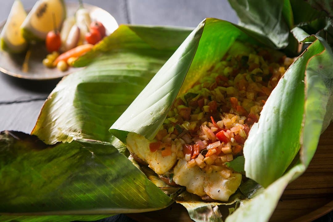 Cooking in leaves, the way the river people always have. Photo: Yvonne Kreuzmayr Fish fillet steamed in a banana leaf packet with a fresh tomato and pepper salsa, served on the aria amazon cruise with a side plate of local chillies, garlic, and tropical fruit