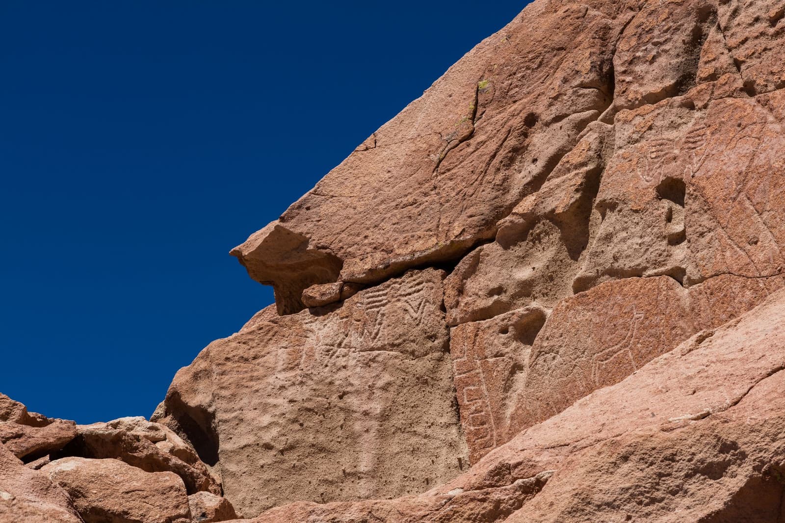 Duizenden jaar oud, en nog steeds het meest intrigerende wat je deze week ziet. Photo: Diego Delso Oude petrogliefen uitgehouwen in een rode vulkanische rotswand tijdens de Atacama woestijn trek, met geometrische symbolen en mensachtige figuren onder een diepblauwe hemel.