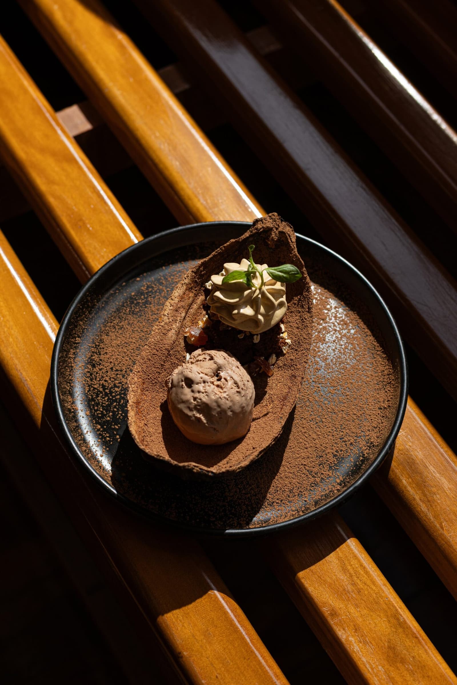 Sobremesa assim merece ser saboreada sem pressa, rio abaixo. Um prato de cerâmica escura polvilhado com cacau sustenta uma bola de sorvete de chocolate e um estilhaço decorativo de chocolate com chantilly e folha de erva fresca, servido sobre ripas de madeira durante o cruzeiro Delfin na Amazônia