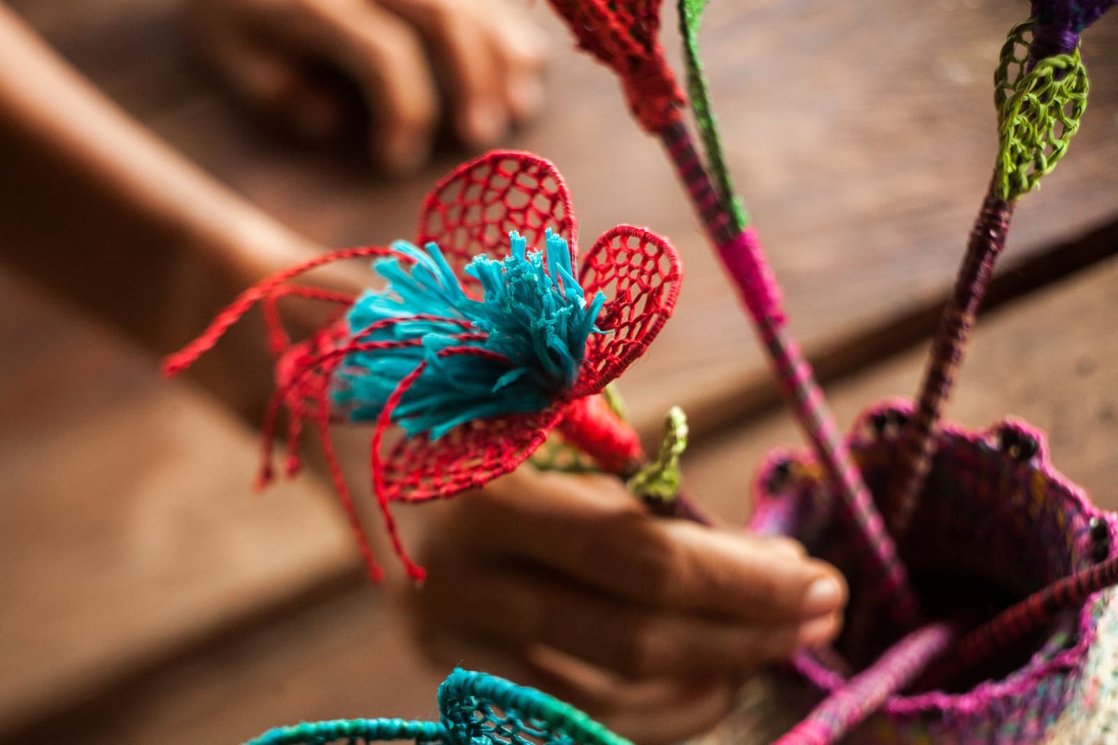 Horas de nós cuidadosos em cada pétala, o mercado da aldeia recompensa quem olha de perto. Photo: er: Rodrigo Rodrich Close-up das mãos de uma criança segurando uma flor de crochê artesanal em fio vermelho e turquesa, parte do artesanato feito pelas mulheres da comunidade de Puerto Miguel durante o cruzeiro pelo Amazonas