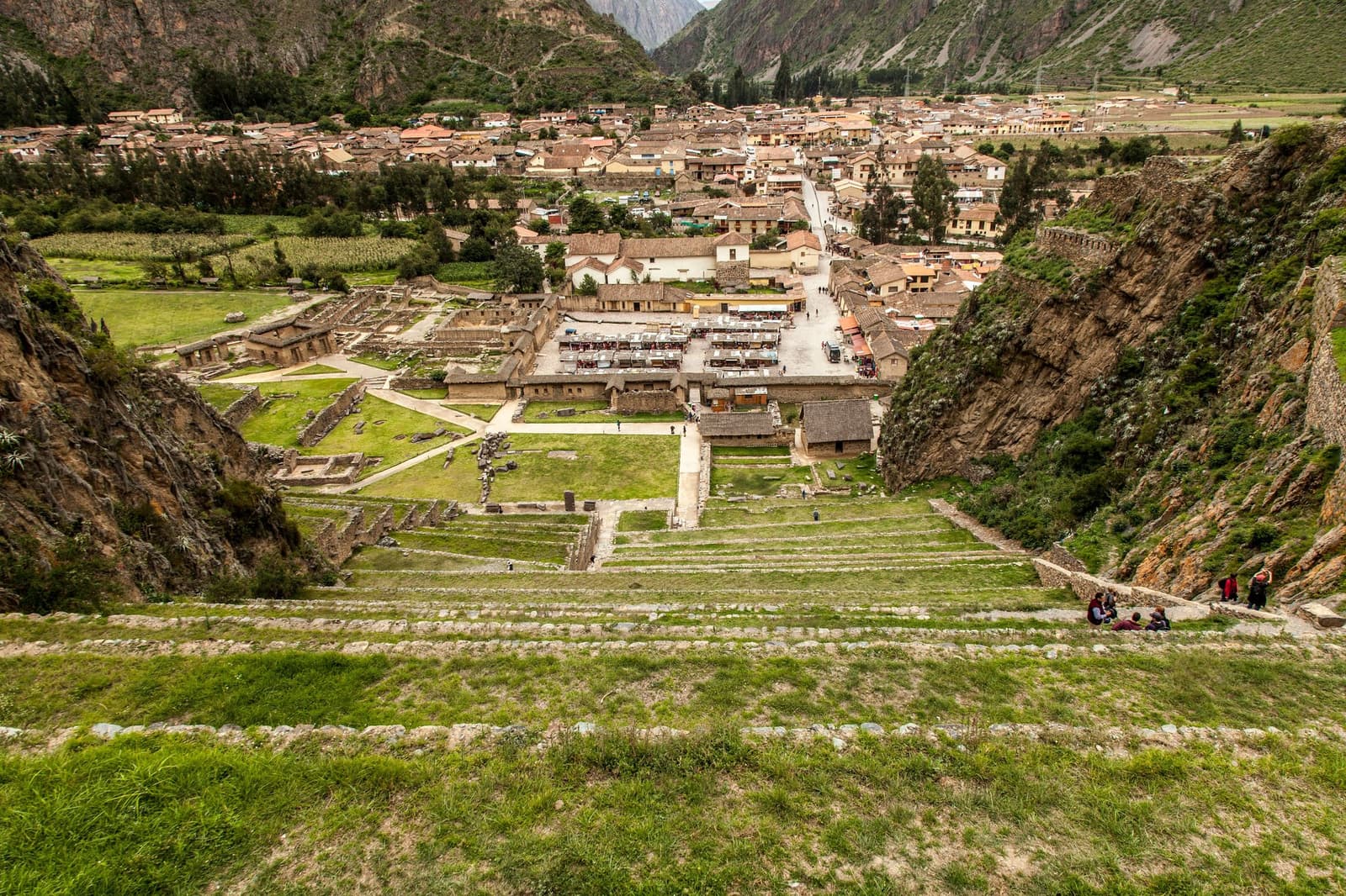 Ollantaytambo: the town grew around the ruins, not the other way around. Aerial view of Ollantaytambo's ancient Inca terraces and ceremonial plaza on this machu picchu amazon tour, with the modern town and Andean valley walls stretching into the distance