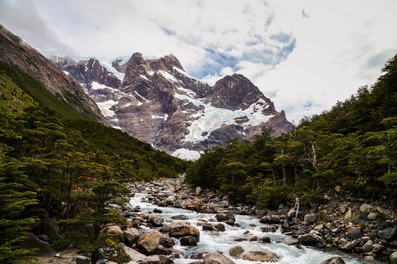 Cold water, loud company, and a glacier waiting at the top of the valley. Photo: WWW.SOTOFOTOS.COM A glacial meltwater river rushing over boulders through lenga beech forest on the self-guided W Trek, with a hanging glacier and jagged snow-covered peaks filling the valley head