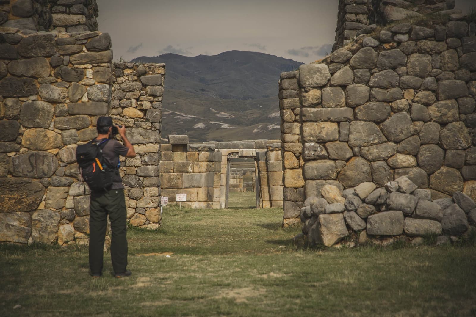 Portas dentro de portas, montanhas dentro de montanhas. O Peru não pressa a revelação. Um mochileiro fotografa uma série de portais de pedra antigos alinhados na trilha Ancascocha, com as montanhas dos Andes visíveis ao fundo