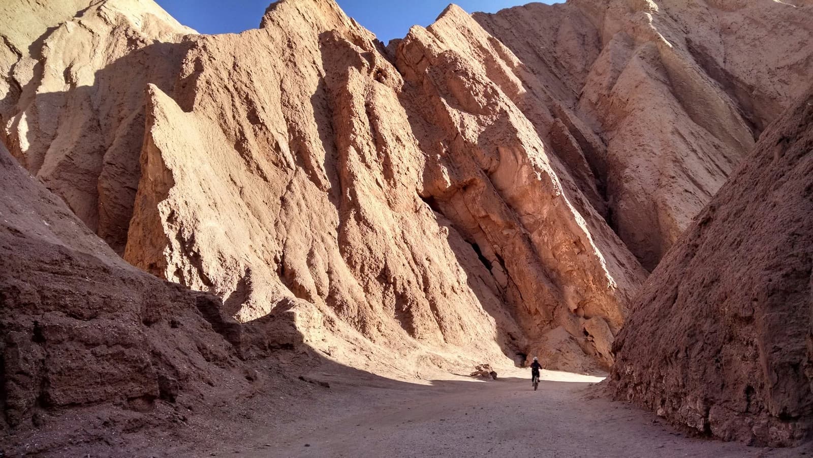 Una persona, un cañón descomunal. La bici pone las cosas en perspectiva. Un ciclista solitario avanza por un estrecho corredor de cañón con altas paredes de roca erosionada en tonos ocre y óxido durante una expedición de camping en el desierto de Atacama en el norte de Chile