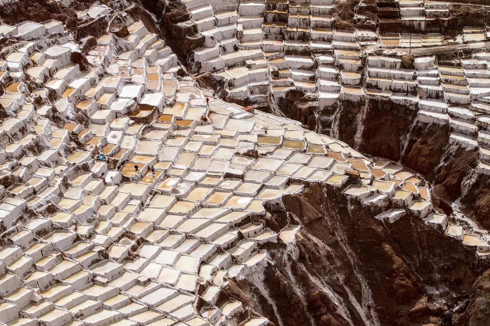 Sal colhido aqui antes mesmo dos Incas, com um processo quase idêntico até hoje. Centenas de terraços de evaporação de sal com bordas brancas descem uma encosta nas salinas de Maras no Vale Sagrado, com pequenas figuras de trabalhadores visíveis entre as piscinas