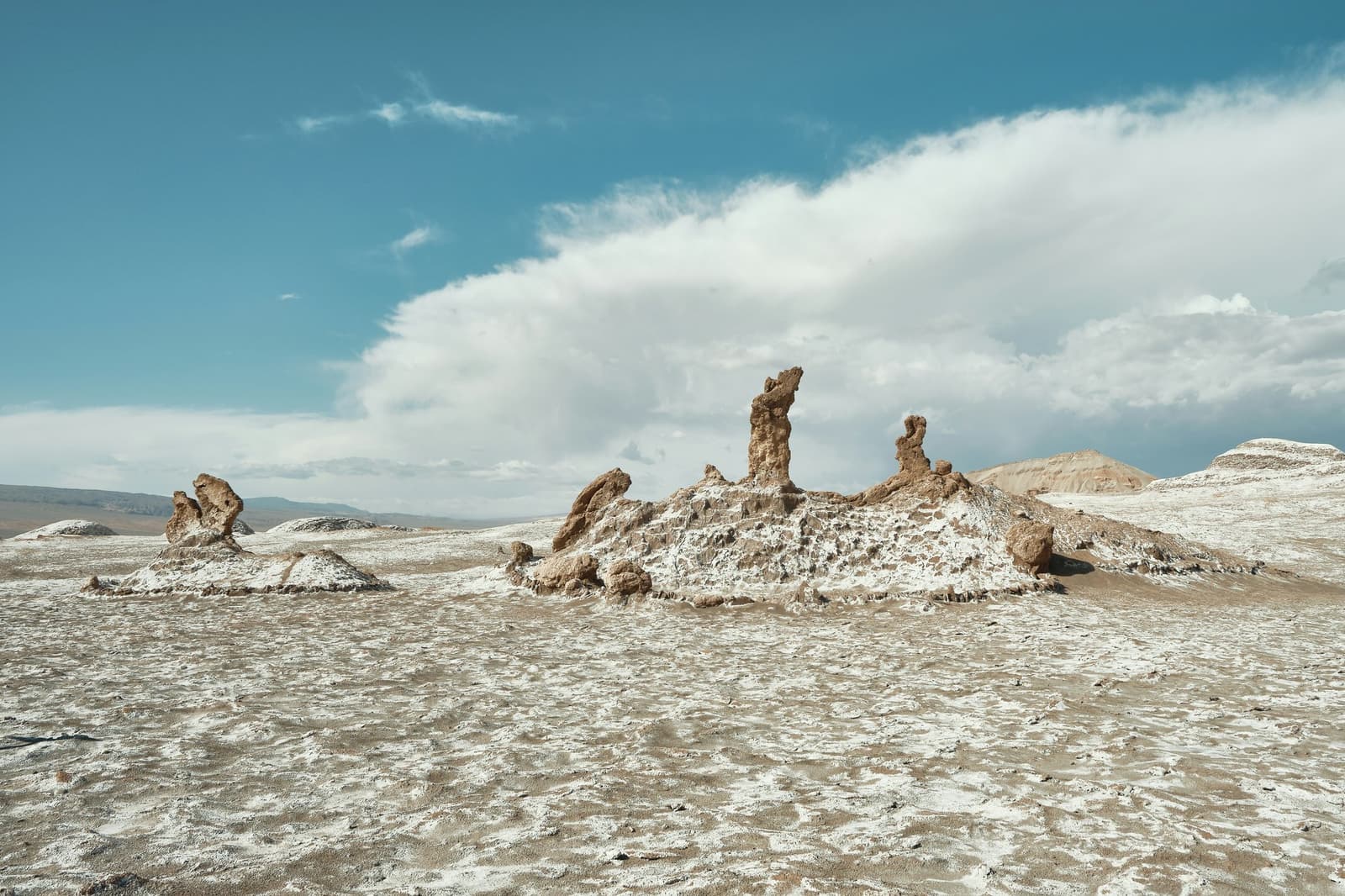 Millones de años de paciencia, esculpidos en algo que el desierto considera un martes cualquiera. Formaciones erosionadas de sal y roca se elevan desde una planicie con costra blanca de sal en el Valle de la Luna, zona de camping en el desierto de Atacama, bajo un amplio cielo azul con nubes