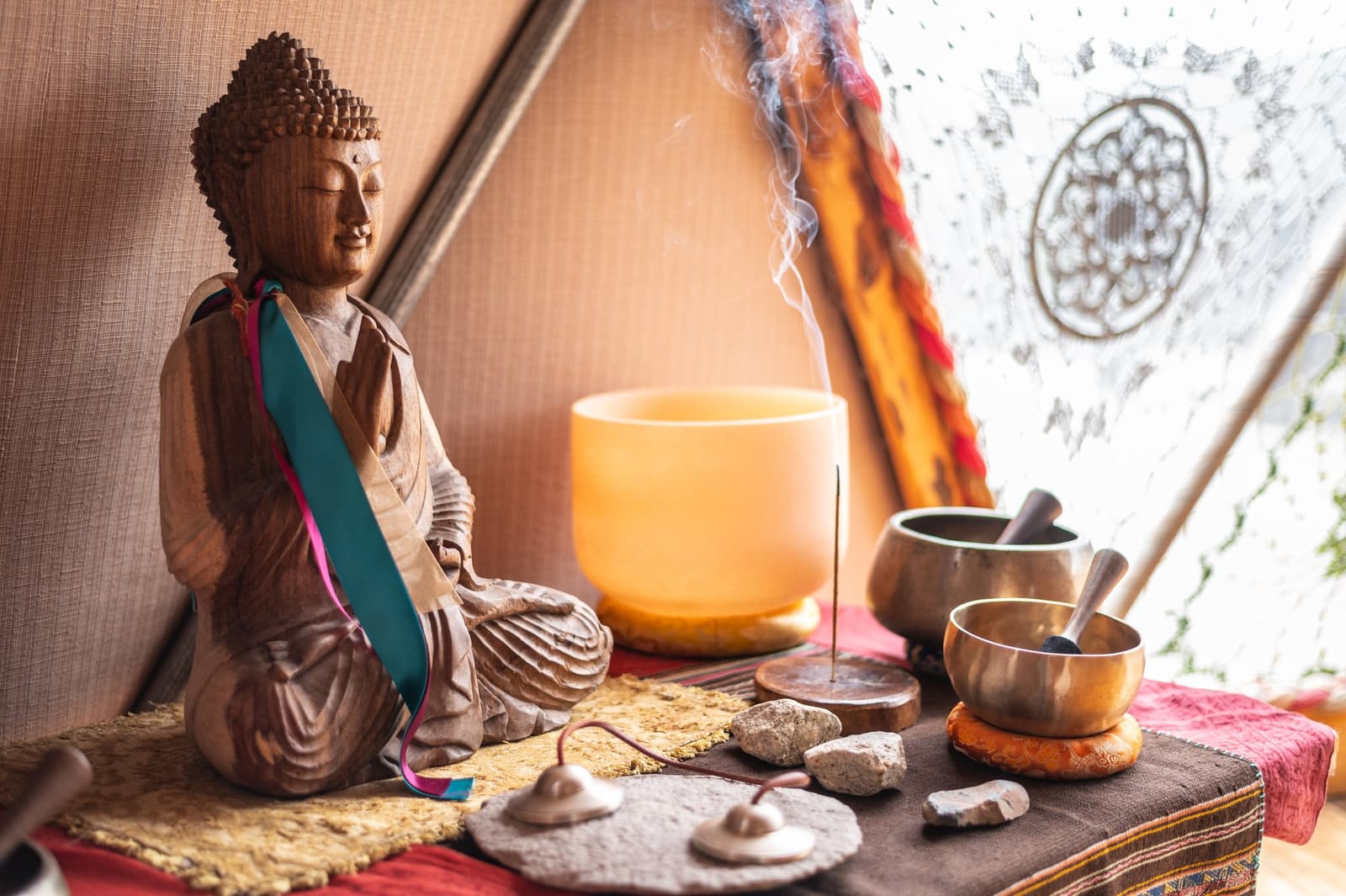 After big days on trail, this little altar has seen some genuine gratitude. Photo: Yoga Dome A carved wooden Buddha statue draped with a teal ribbon sits beside two Tibetan singing bowls, a glowing crystal singing bowl, lit incense, and smooth stones on a layered textile altar inside a dome tent on the o trek patagonia circuit