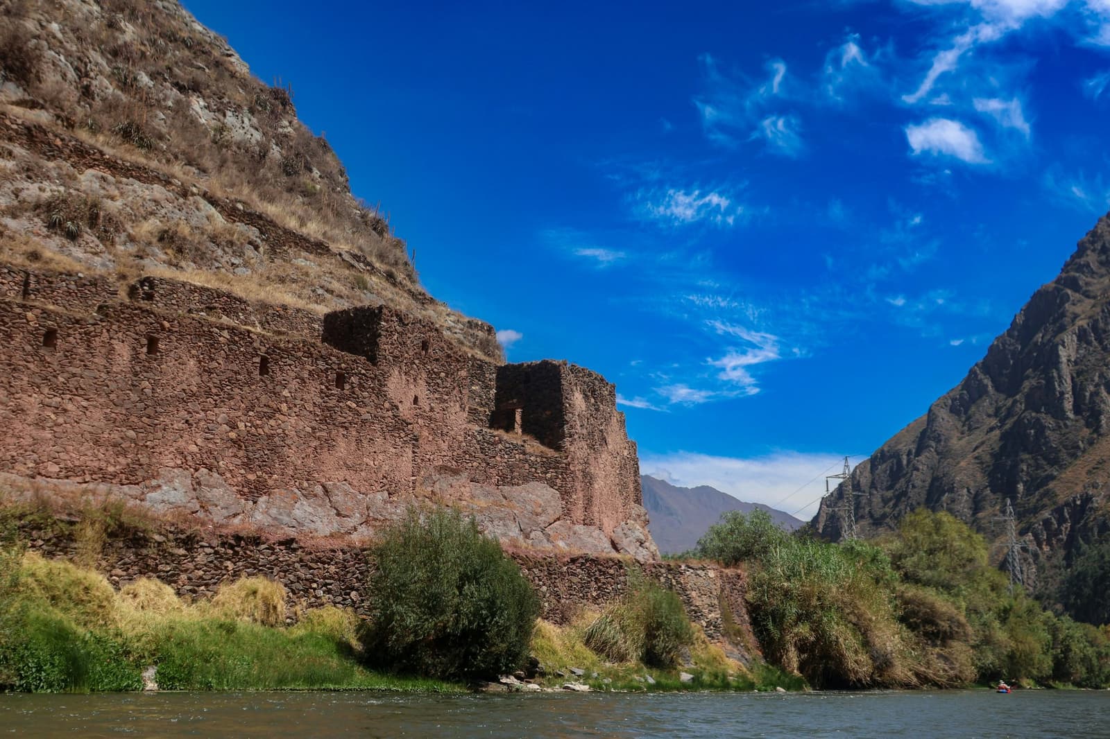 Stone walls that outlasted every empire that tried to ignore them. Ancient stone ruins of a pre-Columbian structure built into a steep canyon cliff above a river, seen from the water on a machu picchu amazon tour machu picchu and amazon tours route through Peru's Andean highlands