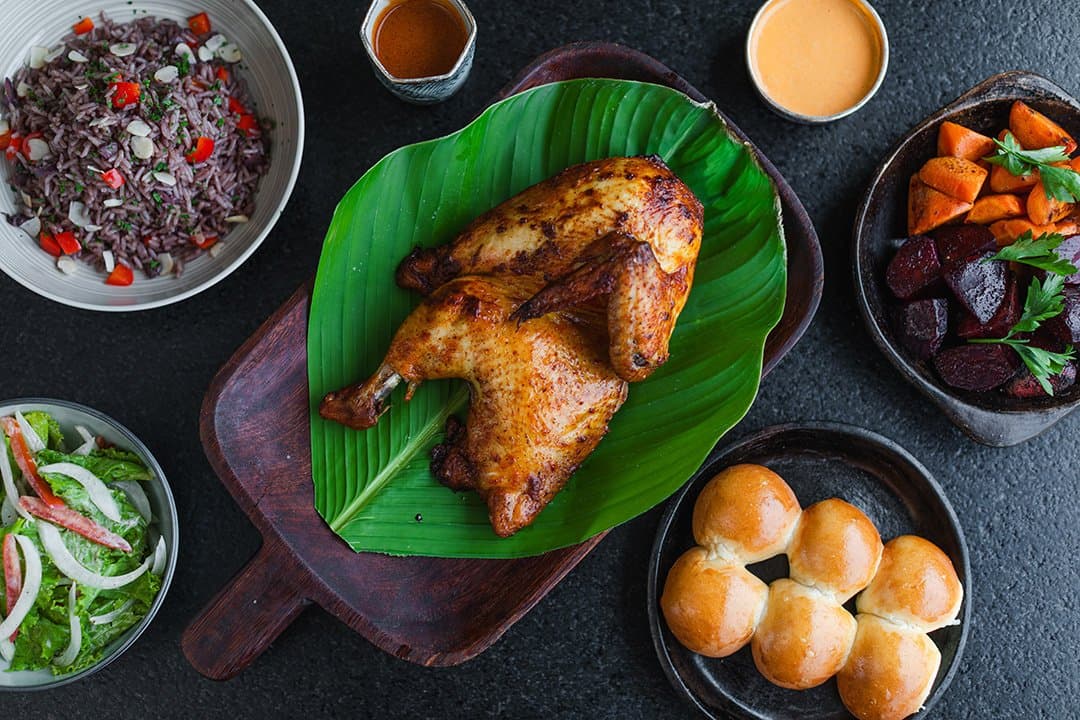 River chicken, banana leaf, and four sides that make the jungle feel close. Photo: Yvonne Kreuzmayr A spice-rubbed roasted chicken on a banana leaf–lined wooden board, surrounded by purple rice with almonds and red pepper, roasted root vegetables with beets, fresh rolls, a green salad, and two dipping sauces, served aboard the aria amazon cruise