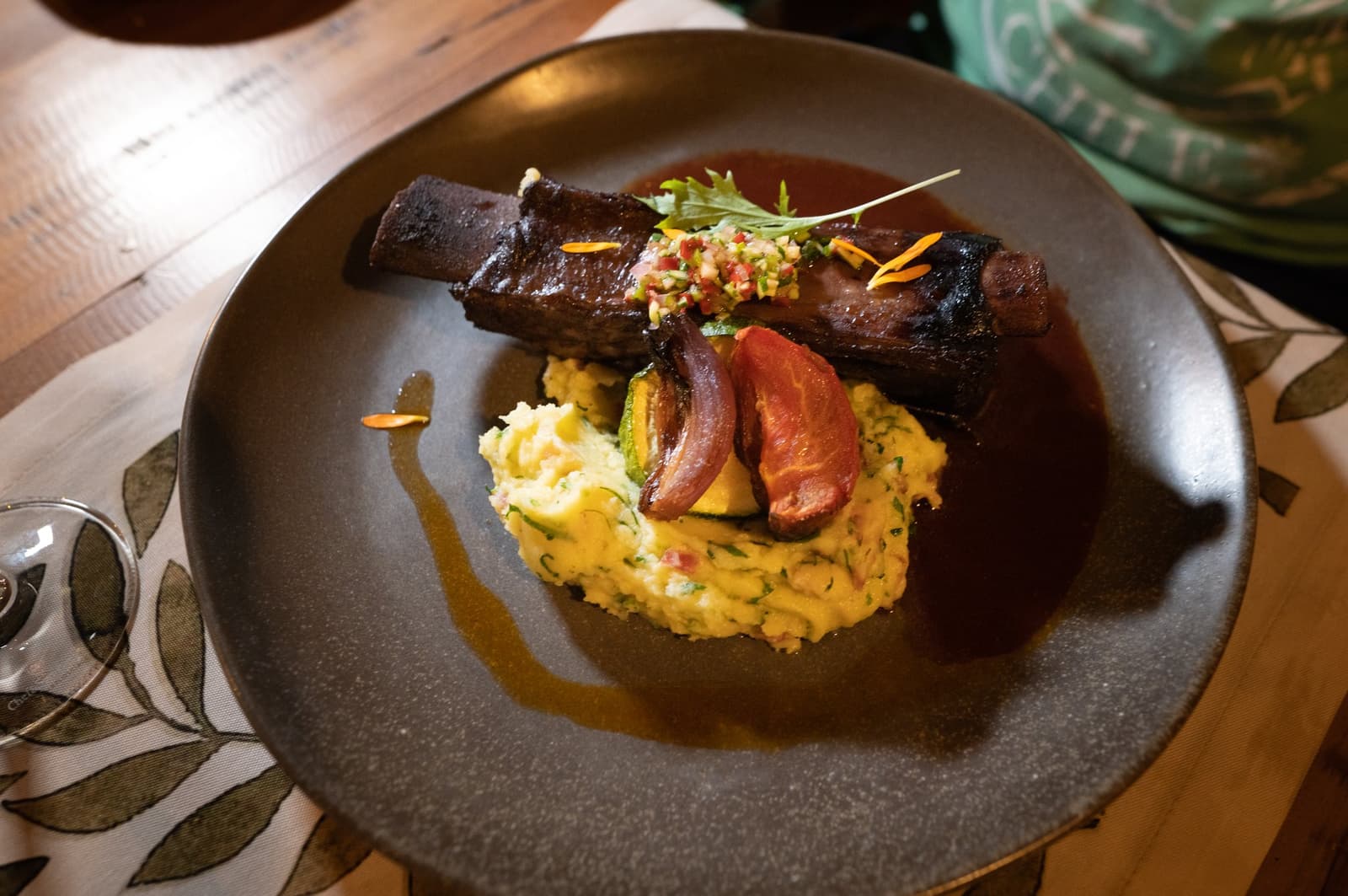 After a day on the steppe, this is exactly what the table was set for. A glazed braised short rib served on herb-flecked mashed potato with roasted vegetables and a fresh salsa, plated on a dark ceramic dish at Estancia Cerro Guido's restaurant
