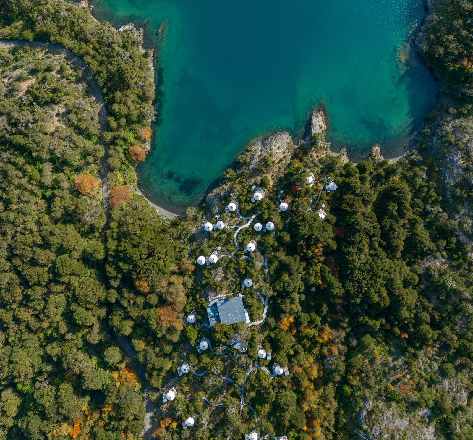 Tucked into the trees so well, you almost have to look twice. Photo: Patagonia Camp Aerial view of Patagonia Camp showing white dome yurts tucked among native lenga forest on a rocky peninsula beside the turquoise waters of Lake Toro in Chilean Patagonia